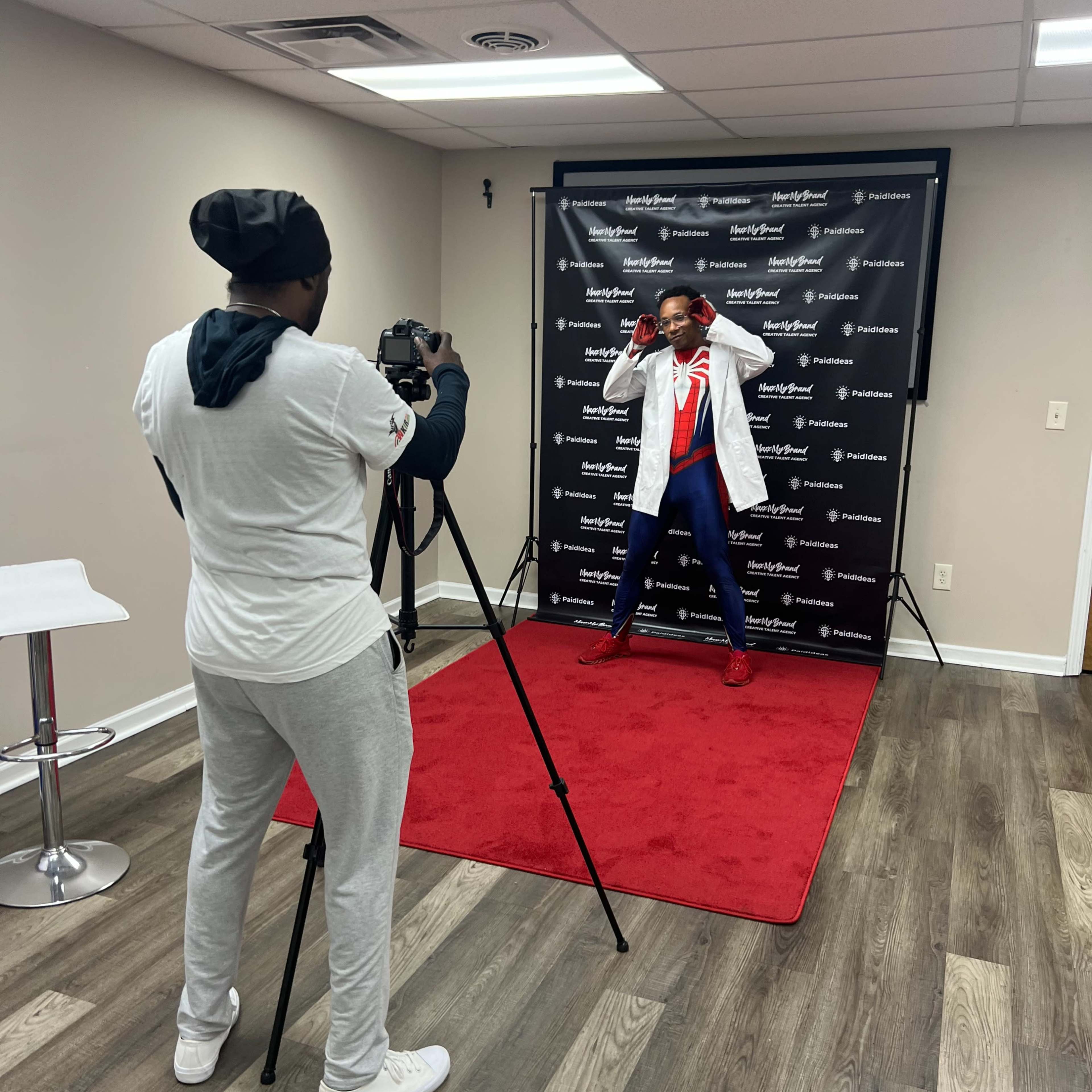 A person in a lab coat poses for a photo in front of a backdrop while another person operates a camera.