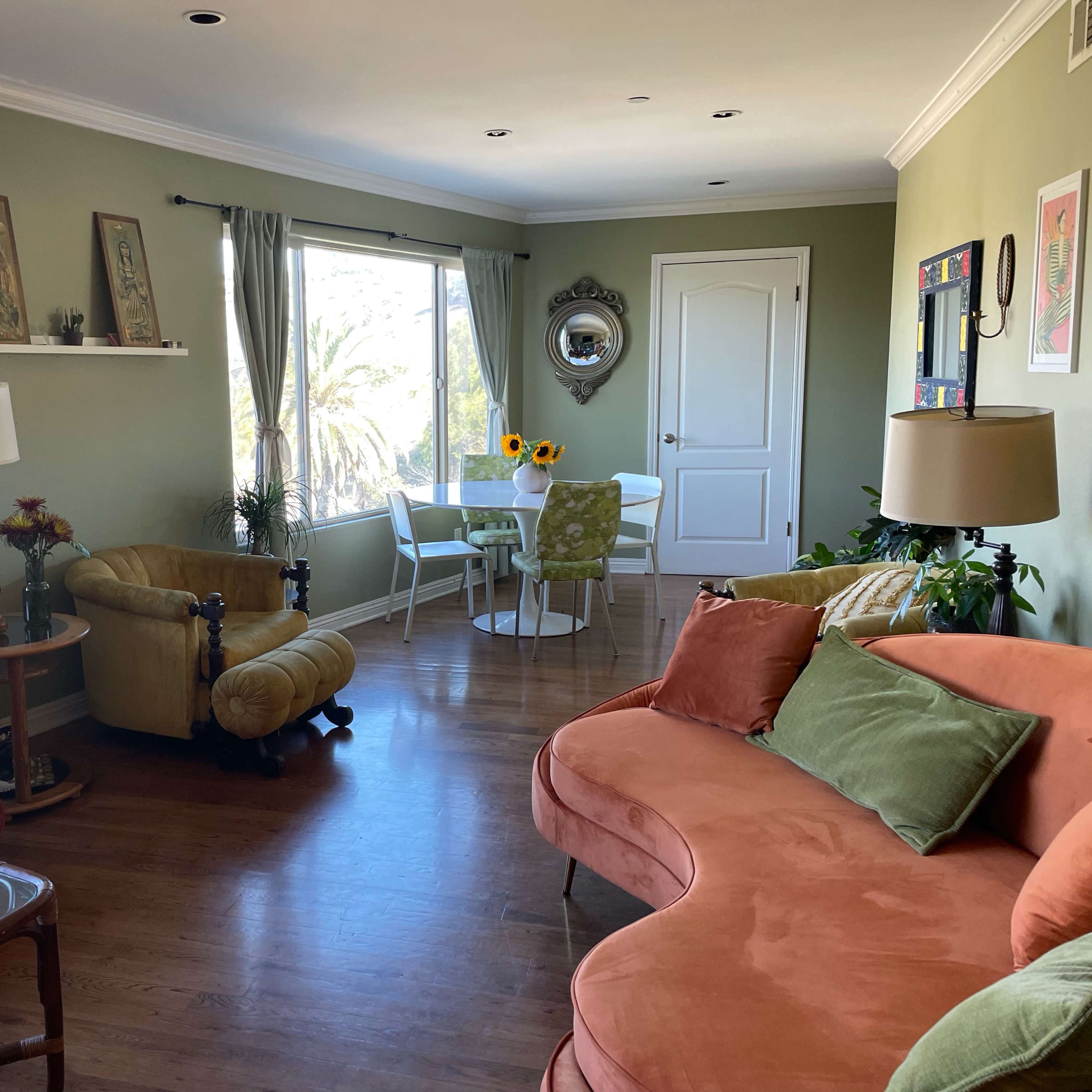 The living room features a mix of orange and green furniture, a dining area with a circular table, and large windows letting in natural light.