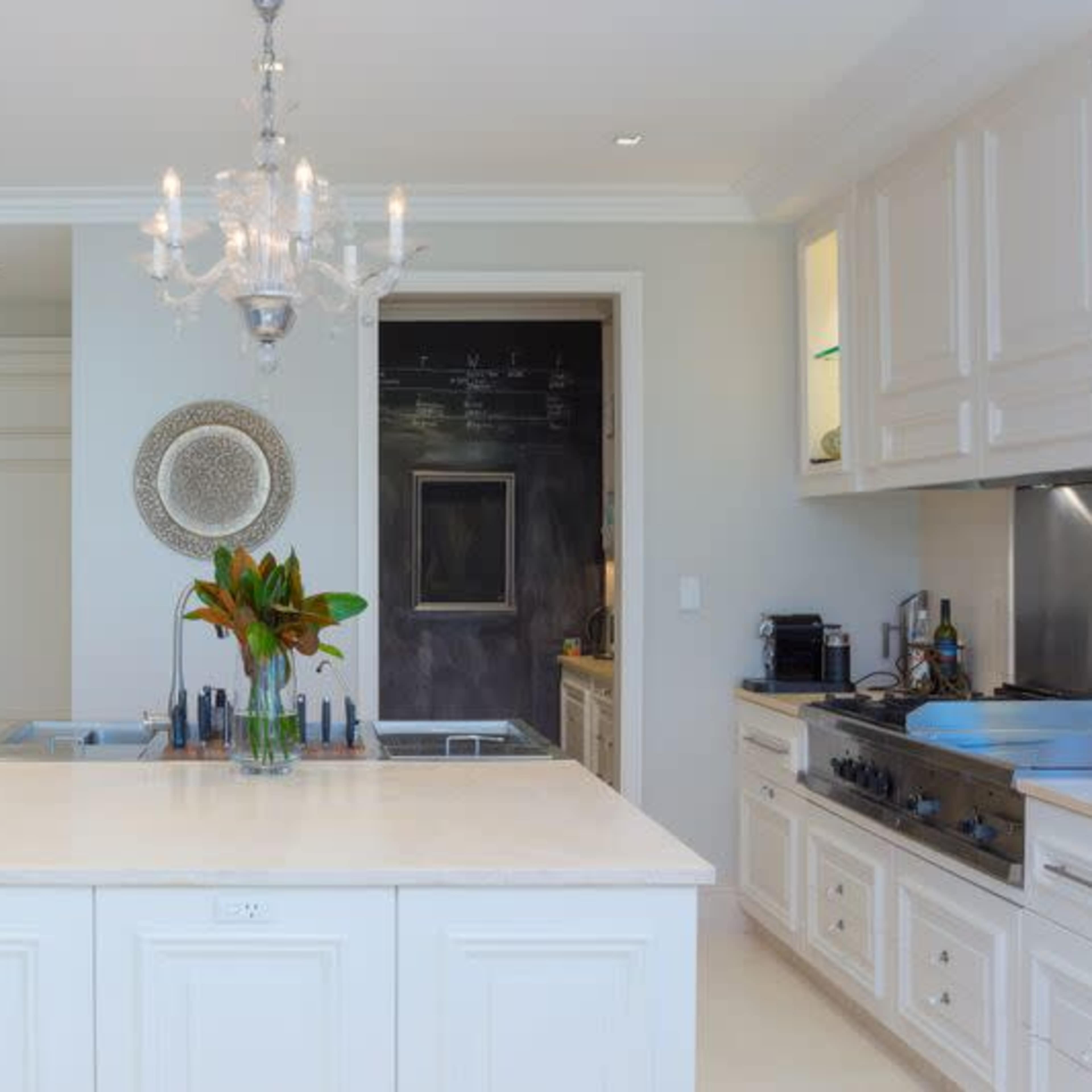 A modern kitchen features an island with a chandelier overhead, built-in ovens, and sleek cabinetry.