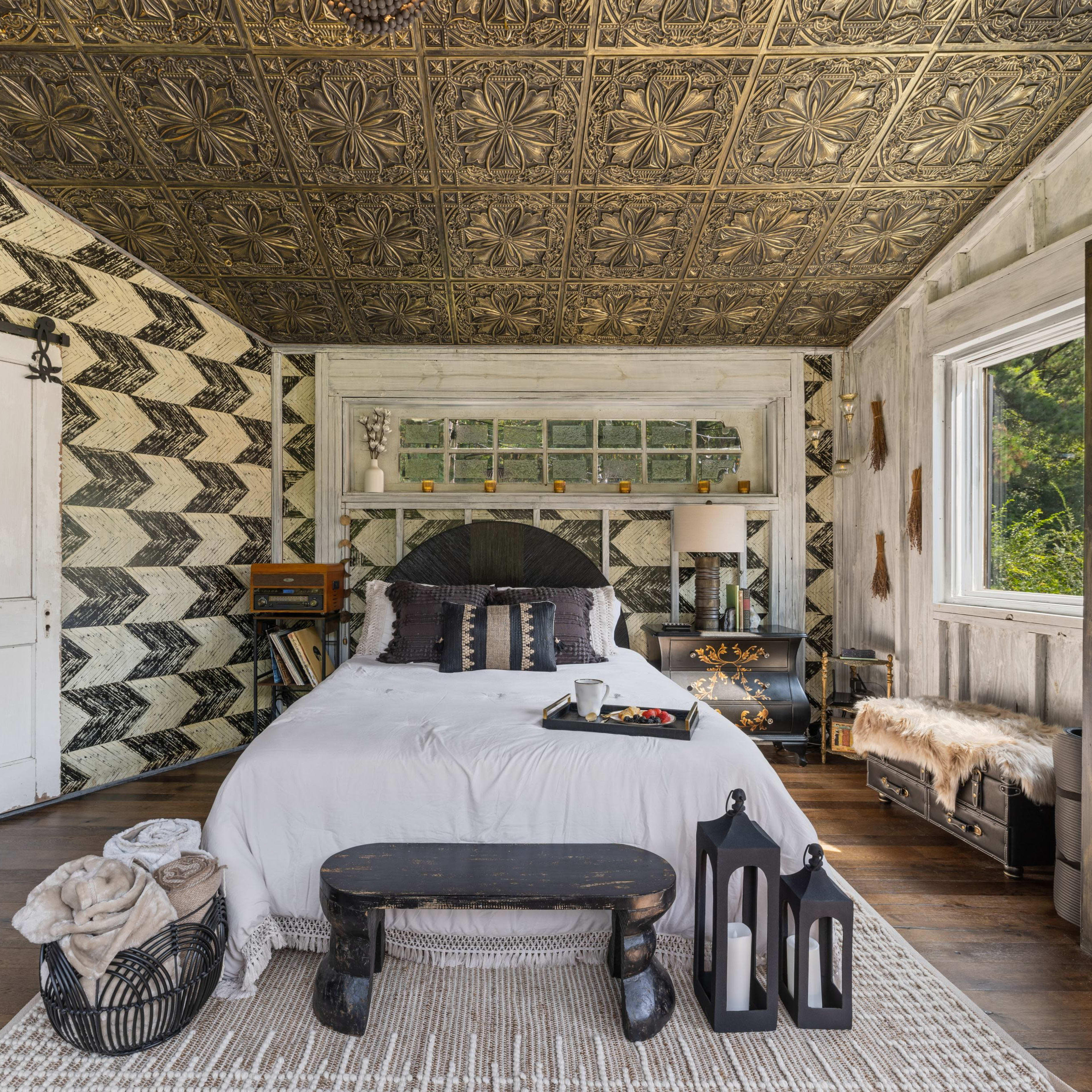 A beautifully designed bedroom featuring a patterned wall, a large bed with decorative pillows, and a mix of rustic and modern furniture.