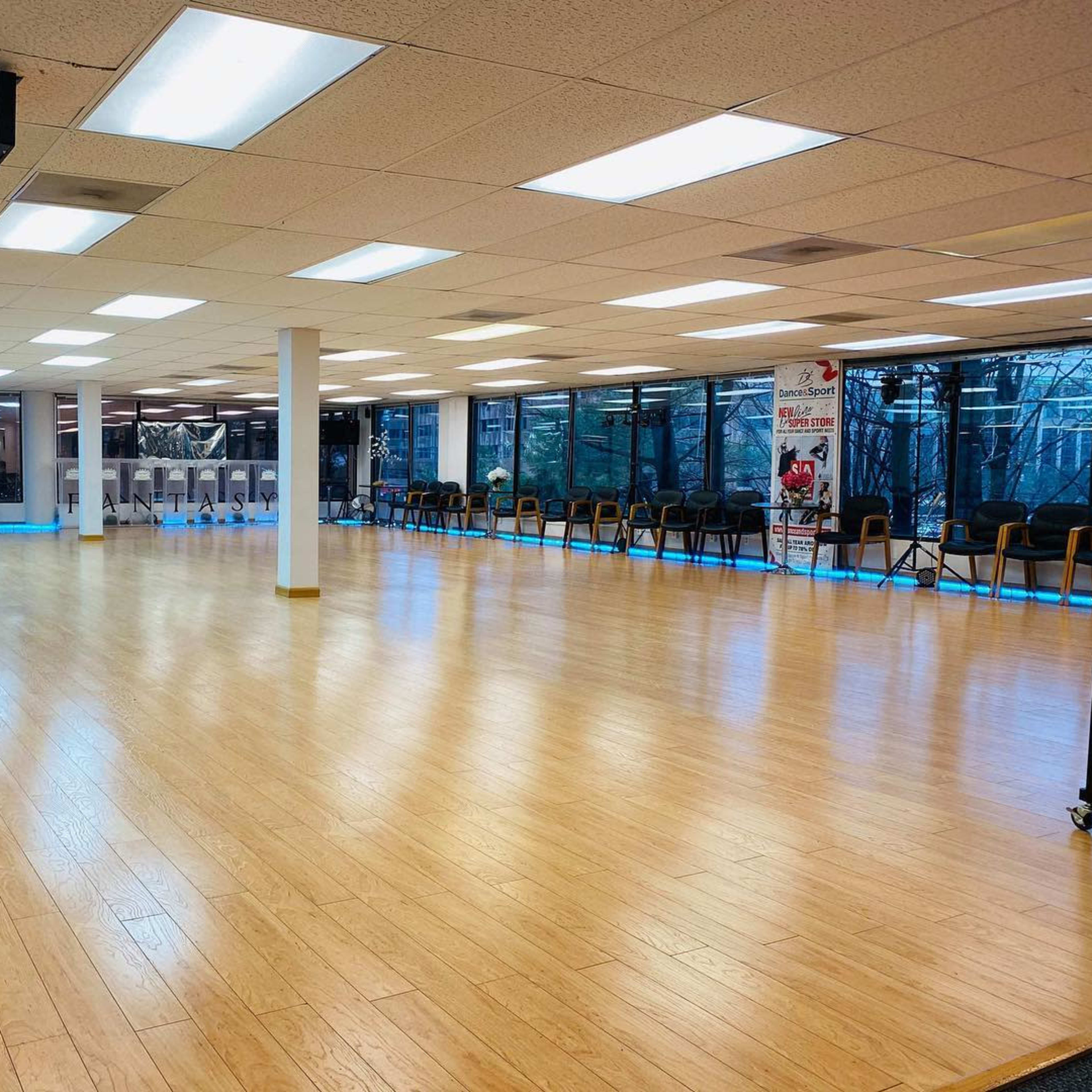 A spacious dance studio with a wooden floor and large windows allowing natural light to fill the room.