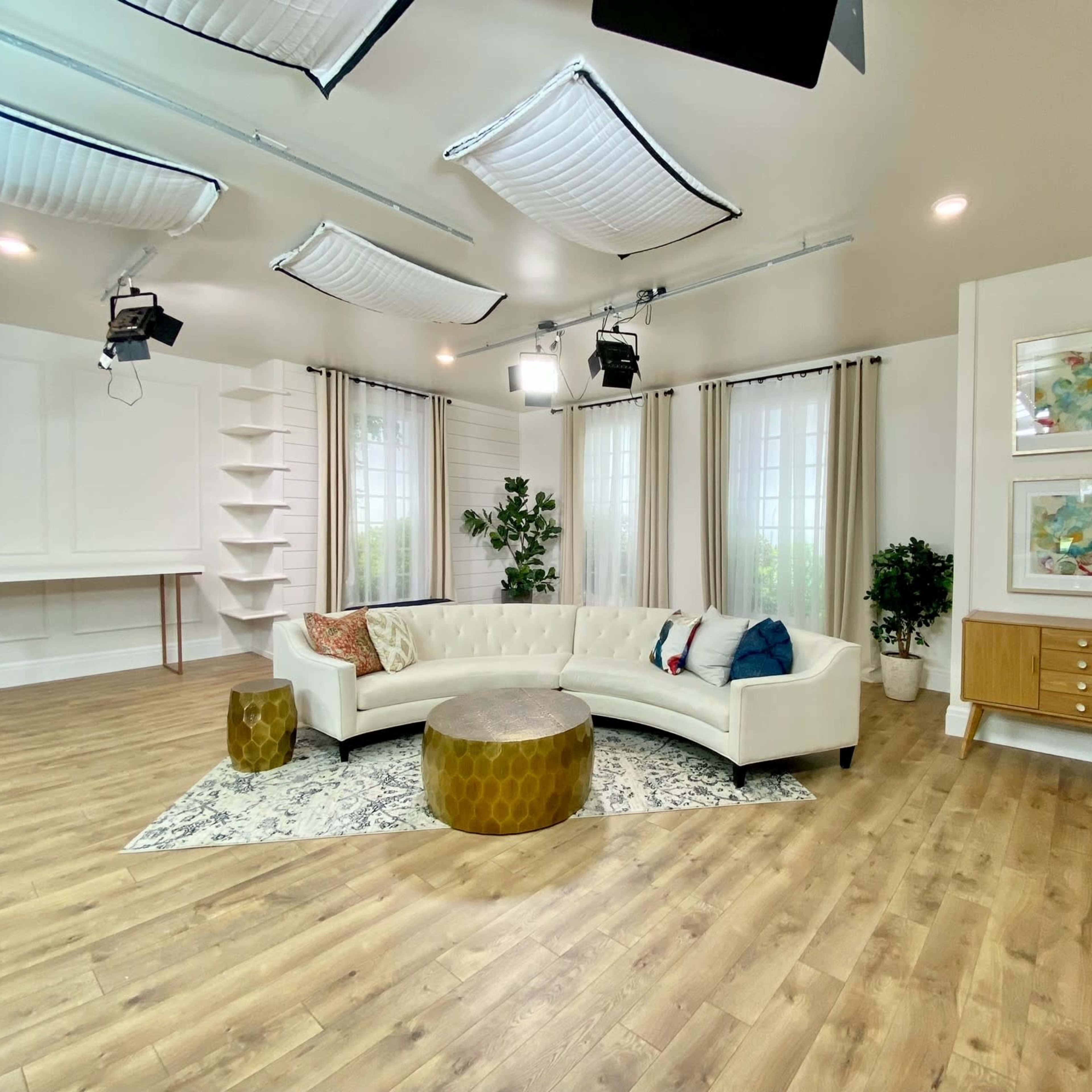 A modern living room with a white sectional sofa, a round gold coffee table, and large windows, complemented by plants and decorative artwork.