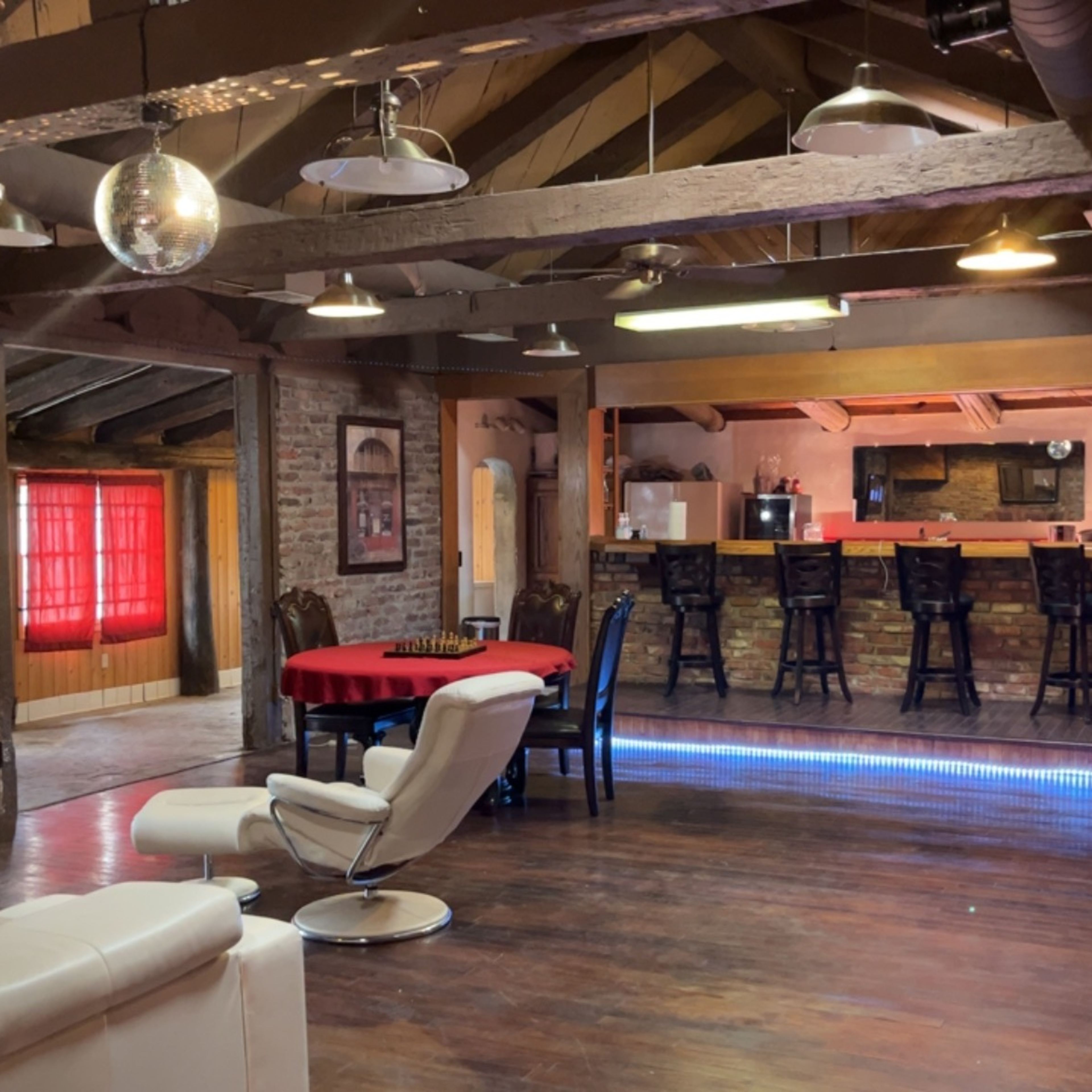 A spacious interior with a bar area, dining table, and seating arranged under exposed wooden beams and a large disco ball.
