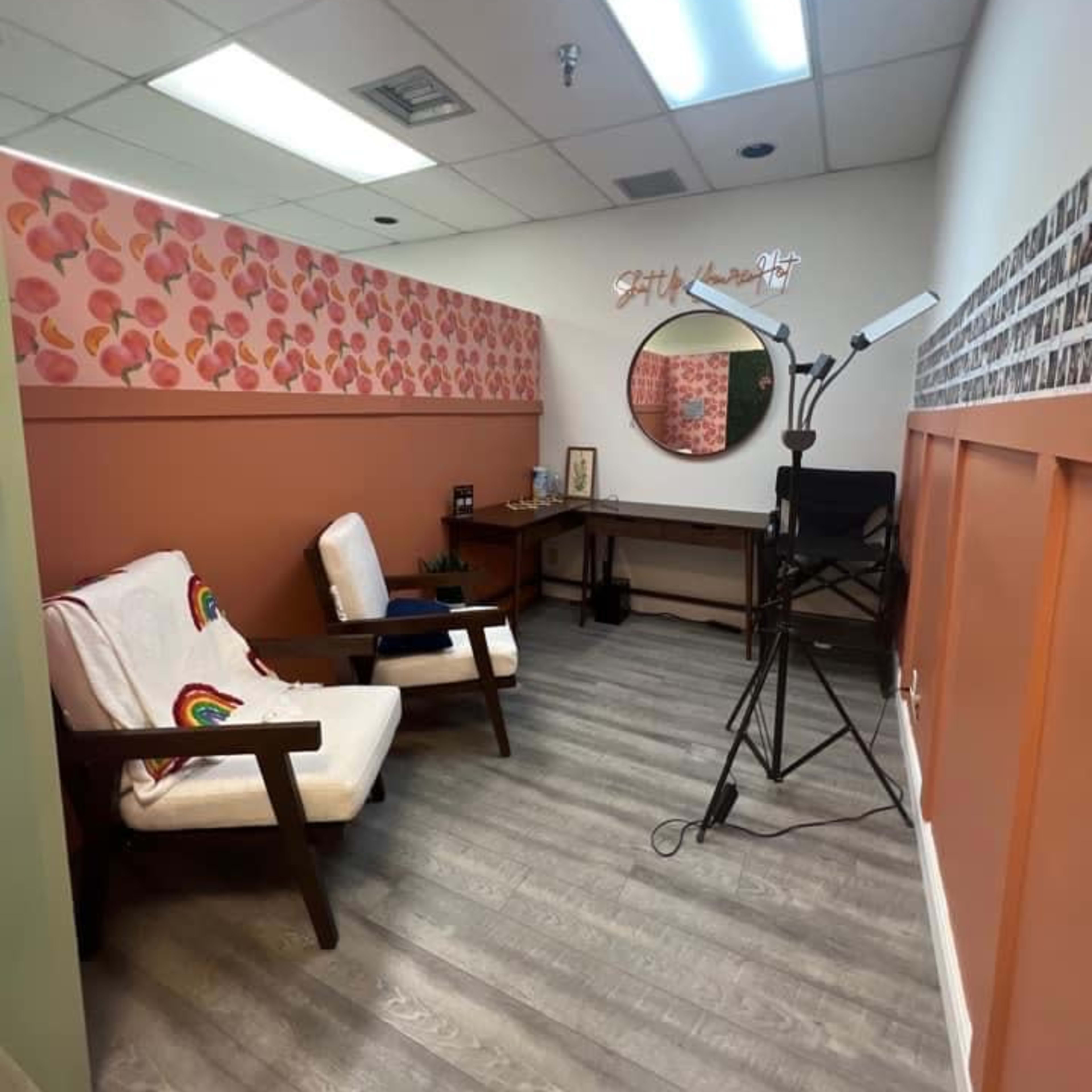 A small, well-lit room with two wooden chairs, a desk, and a ring light set up against patterned walls.