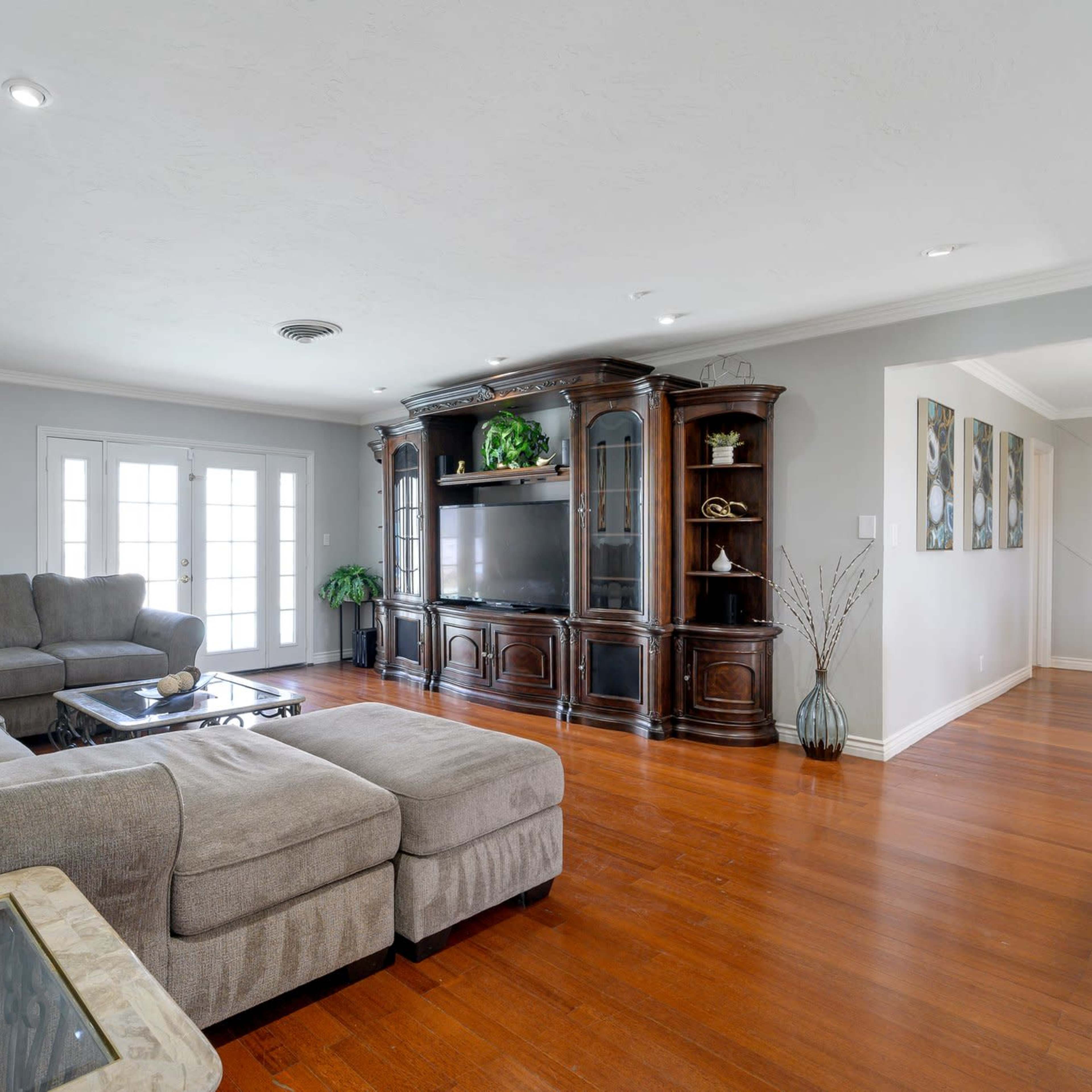 The living room features a large sectional sofa, a wooden entertainment center, and a coffee table, all arranged around a spacious, hardwood floor area.