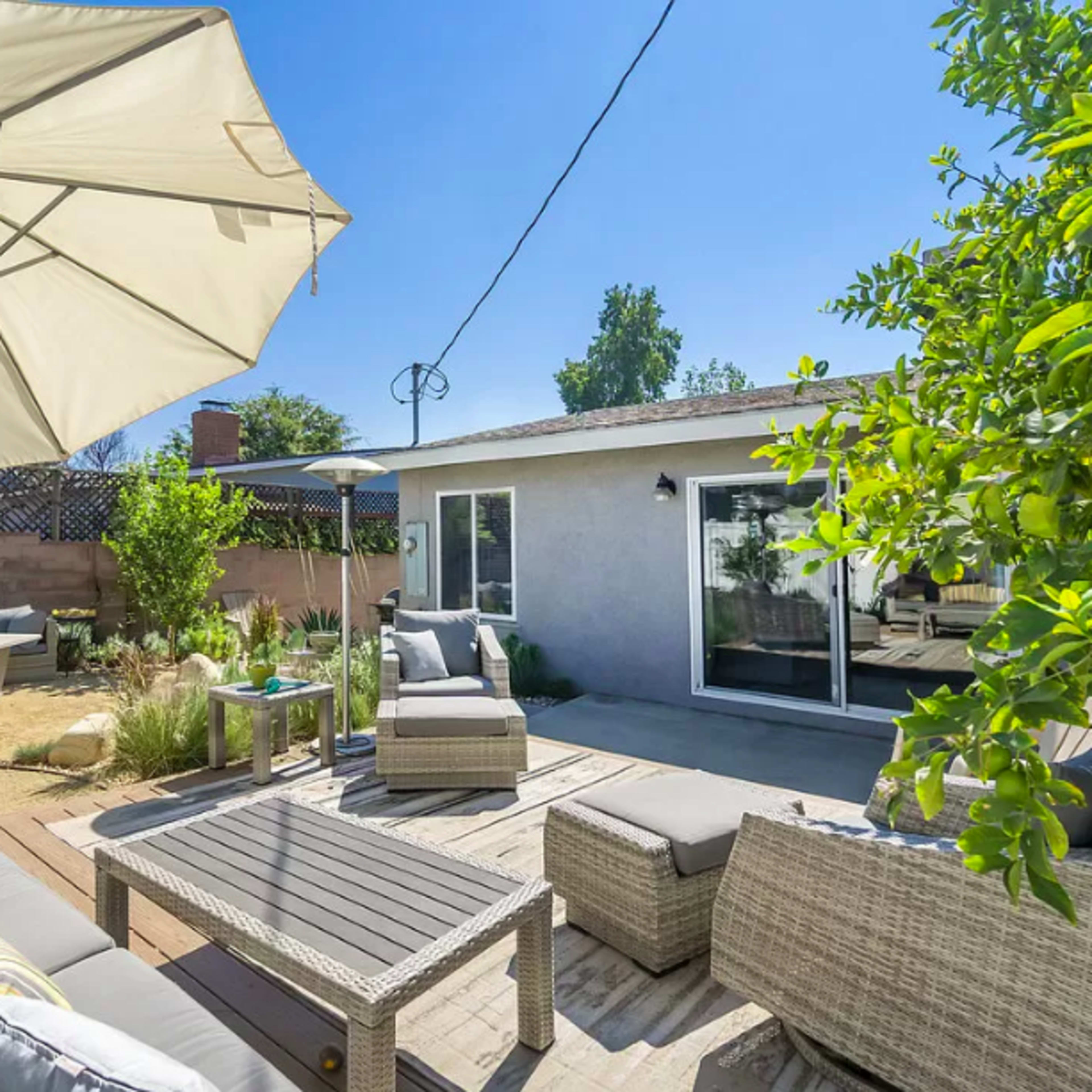 A backyard patio with a gray sofa set, a coffee table, and an umbrella next to a house.