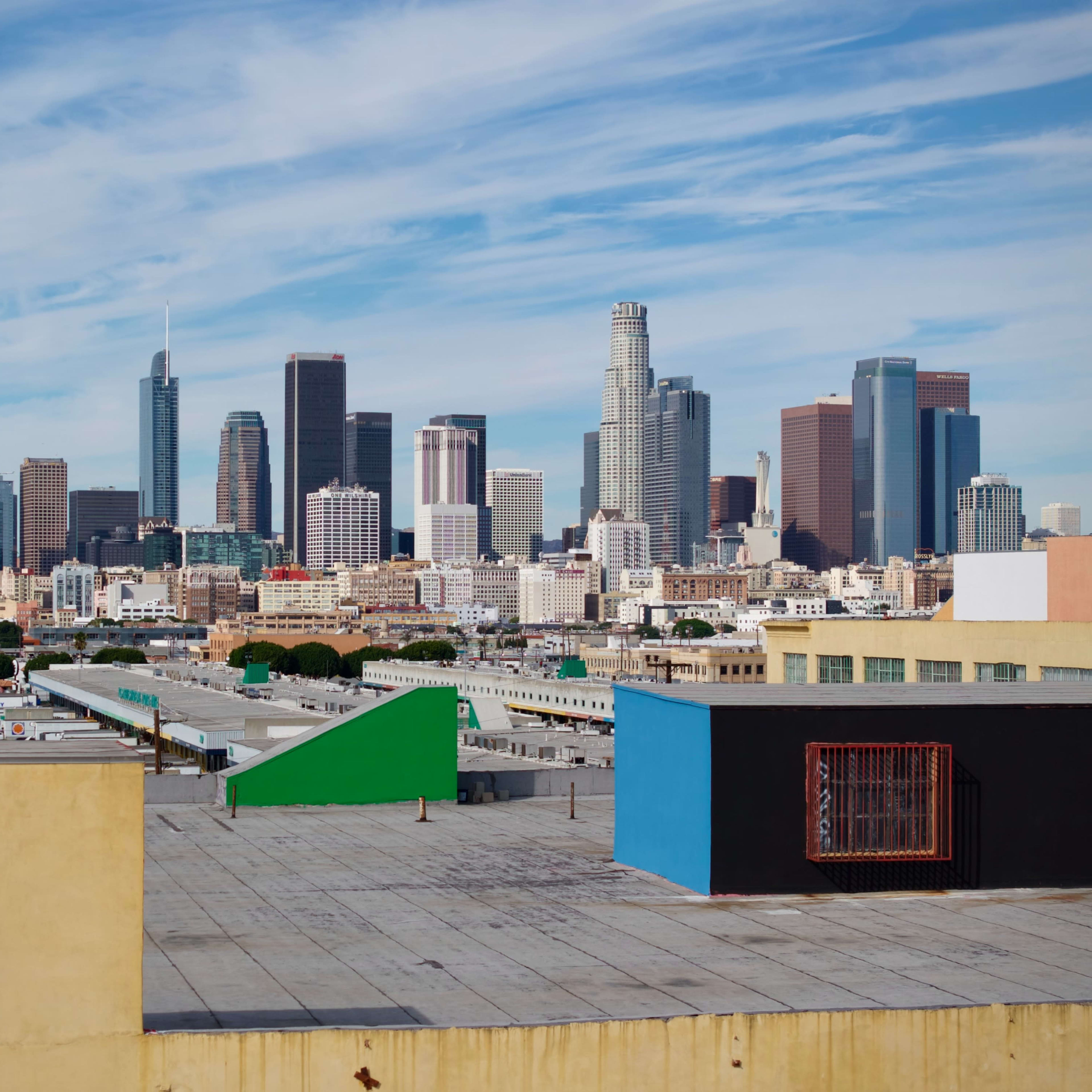 A skyline view of downtown Los Angeles features modern skyscrapers against a blue sky with clouds.