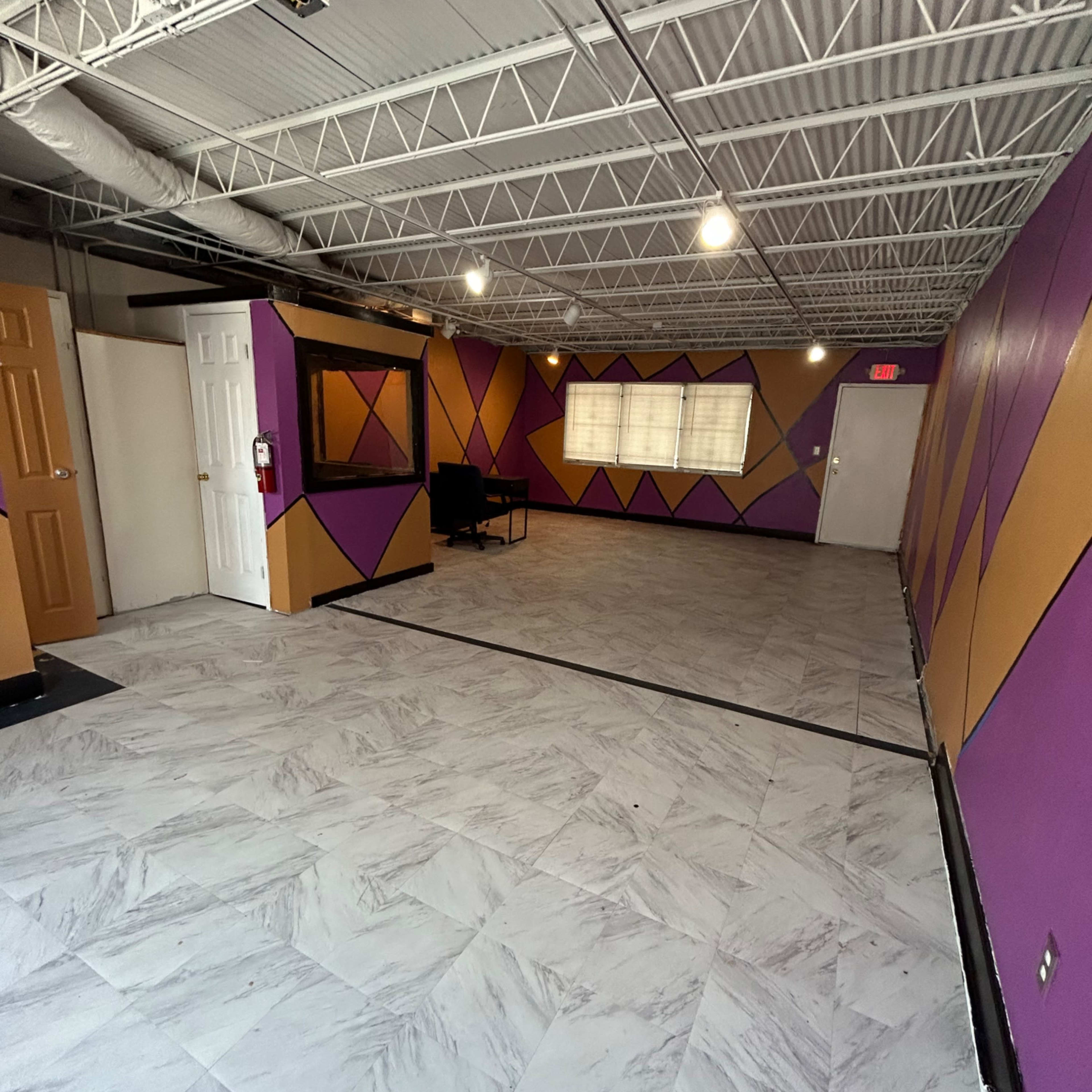 An empty room with patterned purple and orange walls, a tiled floor, and a couple of doors on one side.