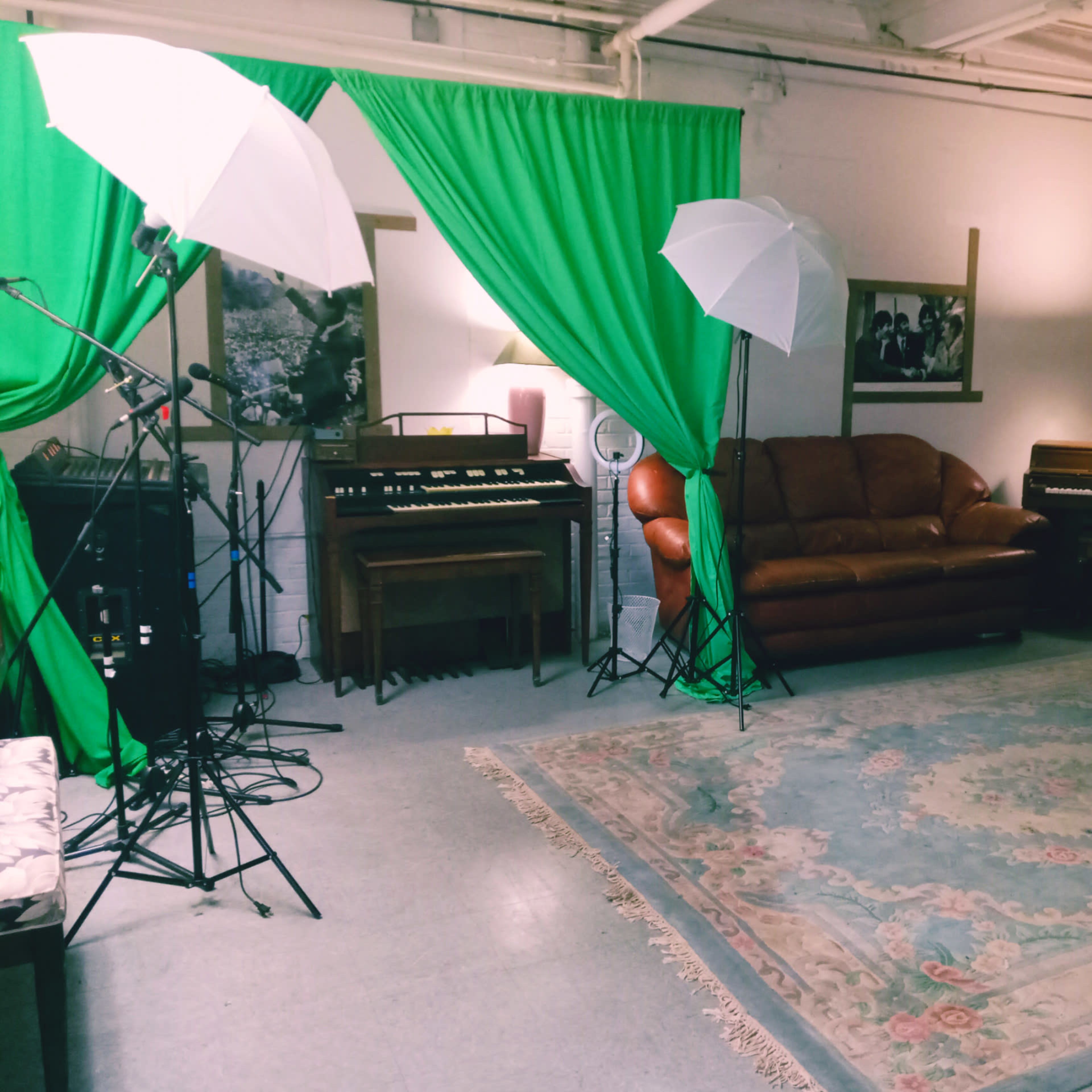 A music recording studio with two umbrellas for lighting, green fabric draping, a sofa, and various keyboards arranged in the space.
