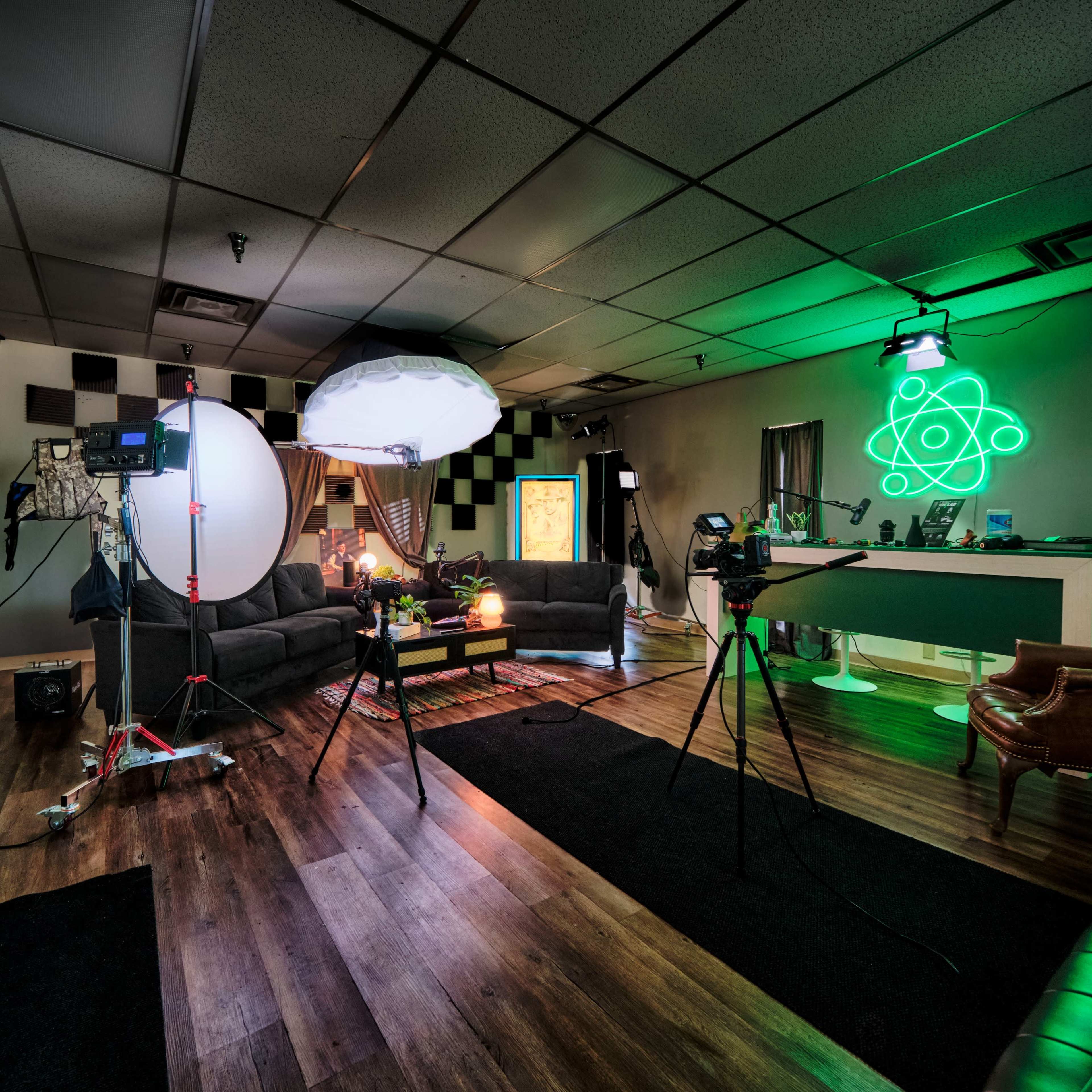 A studio setup with cameras, lighting equipment, and a comfortable seating area featuring black and green decor.