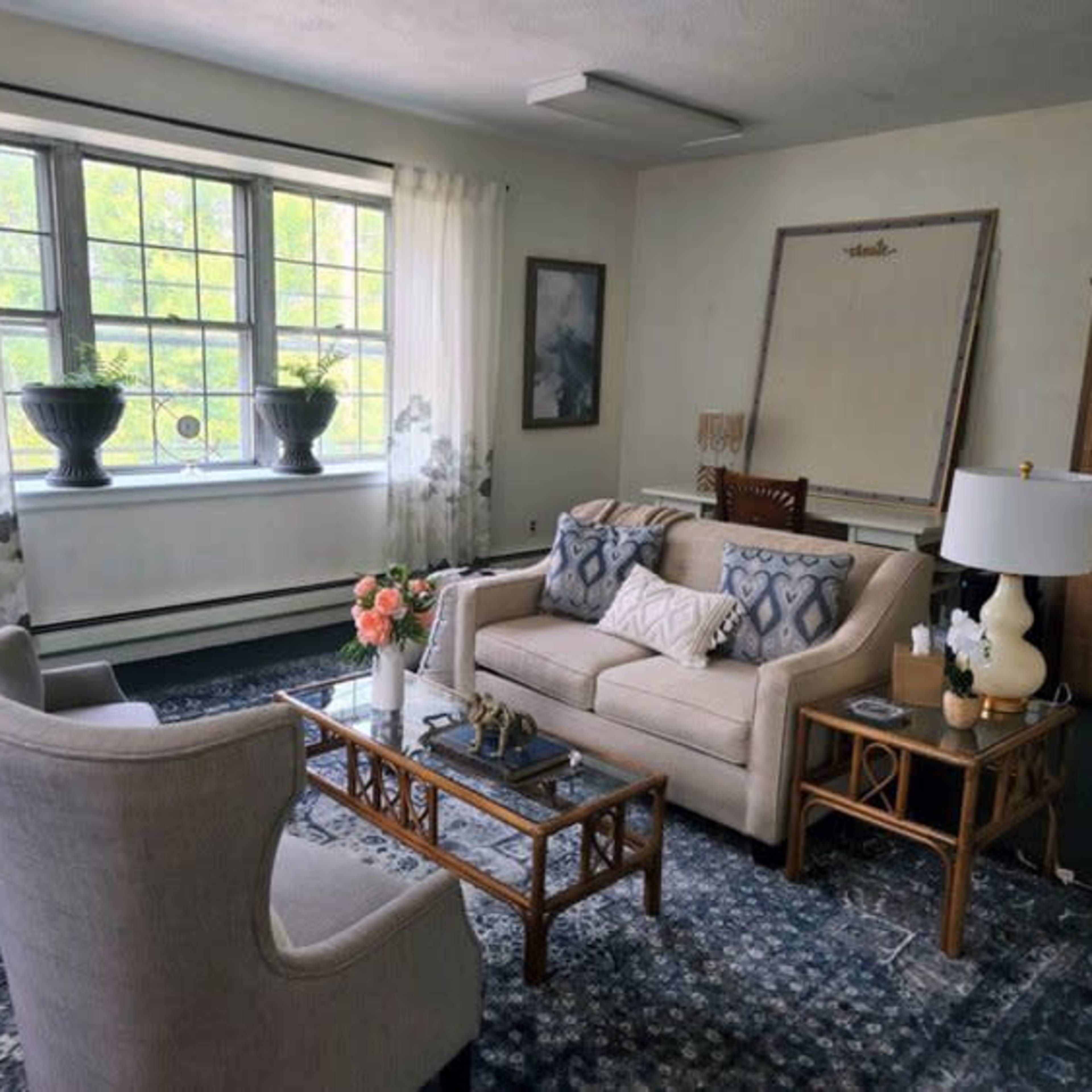 A living room with two armchairs, a sofa, a coffee table, and large windows adorned with sheer curtains.