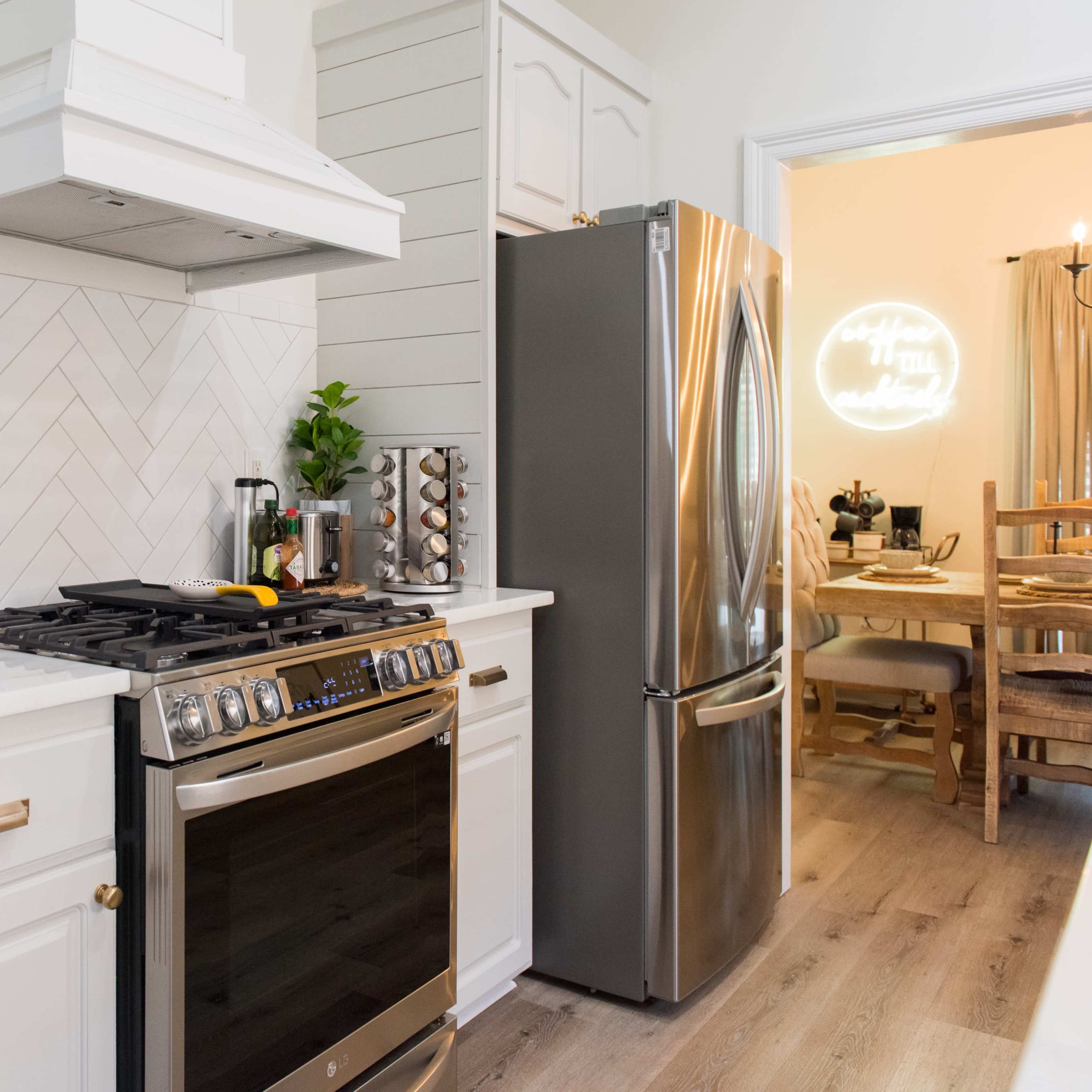 A modern kitchen features a stainless steel stove and refrigerator, herringbone backsplash, and a setup of utensils and spices.