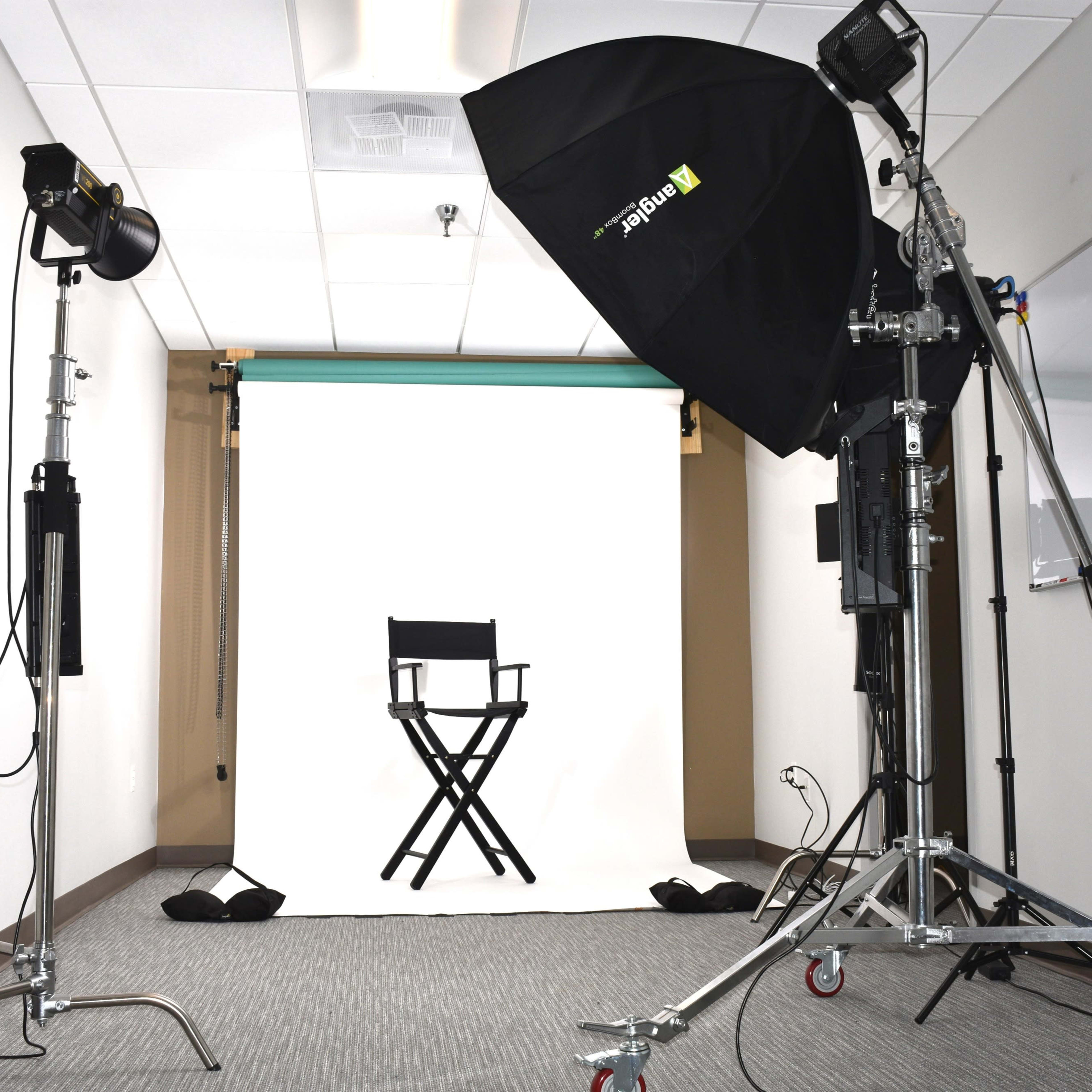 A photography studio setup featuring a blank white backdrop, a director's chair, and professional lighting equipment.