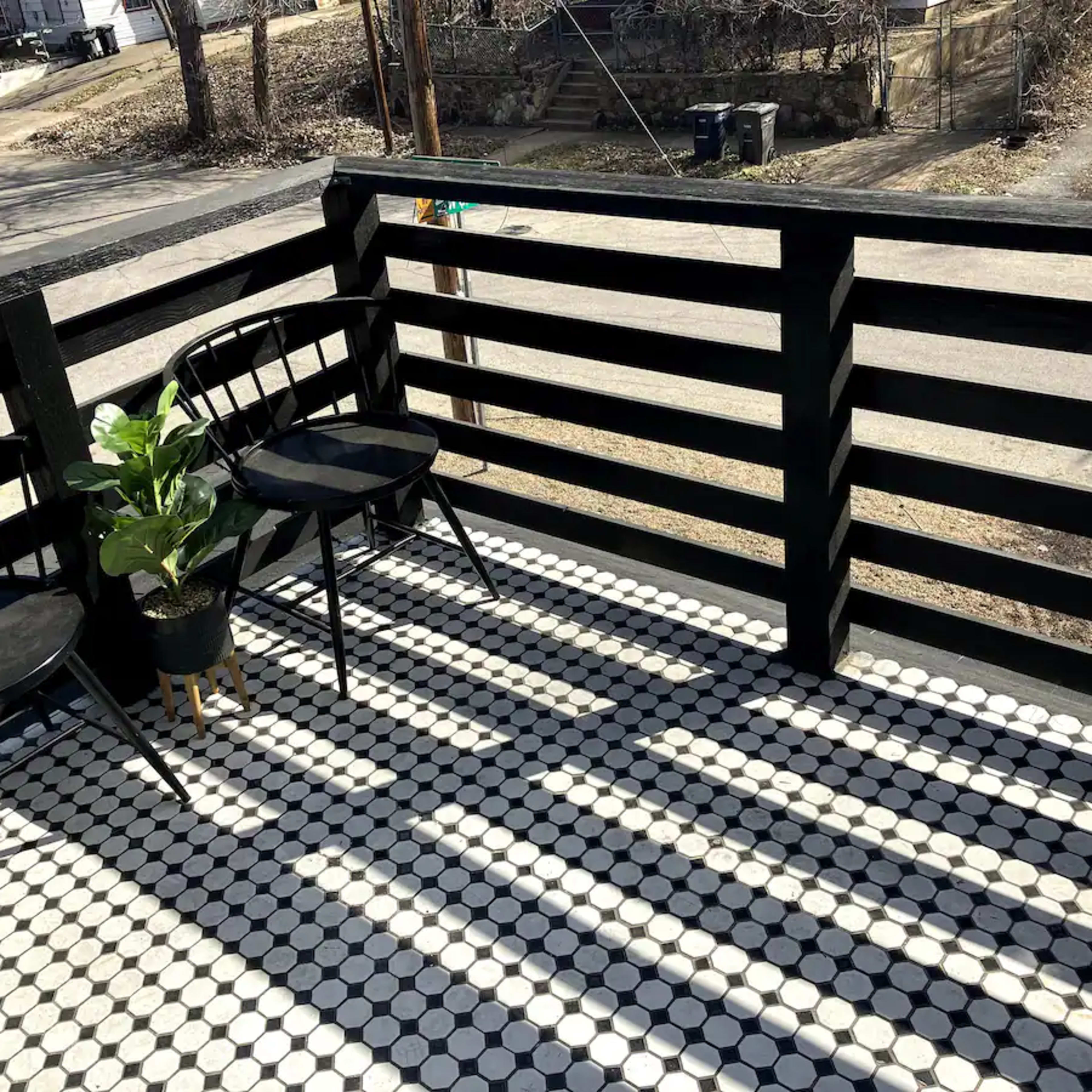 A balcony with two black chairs, a potted plant, and a tiled floor featuring black and white circular patterns.