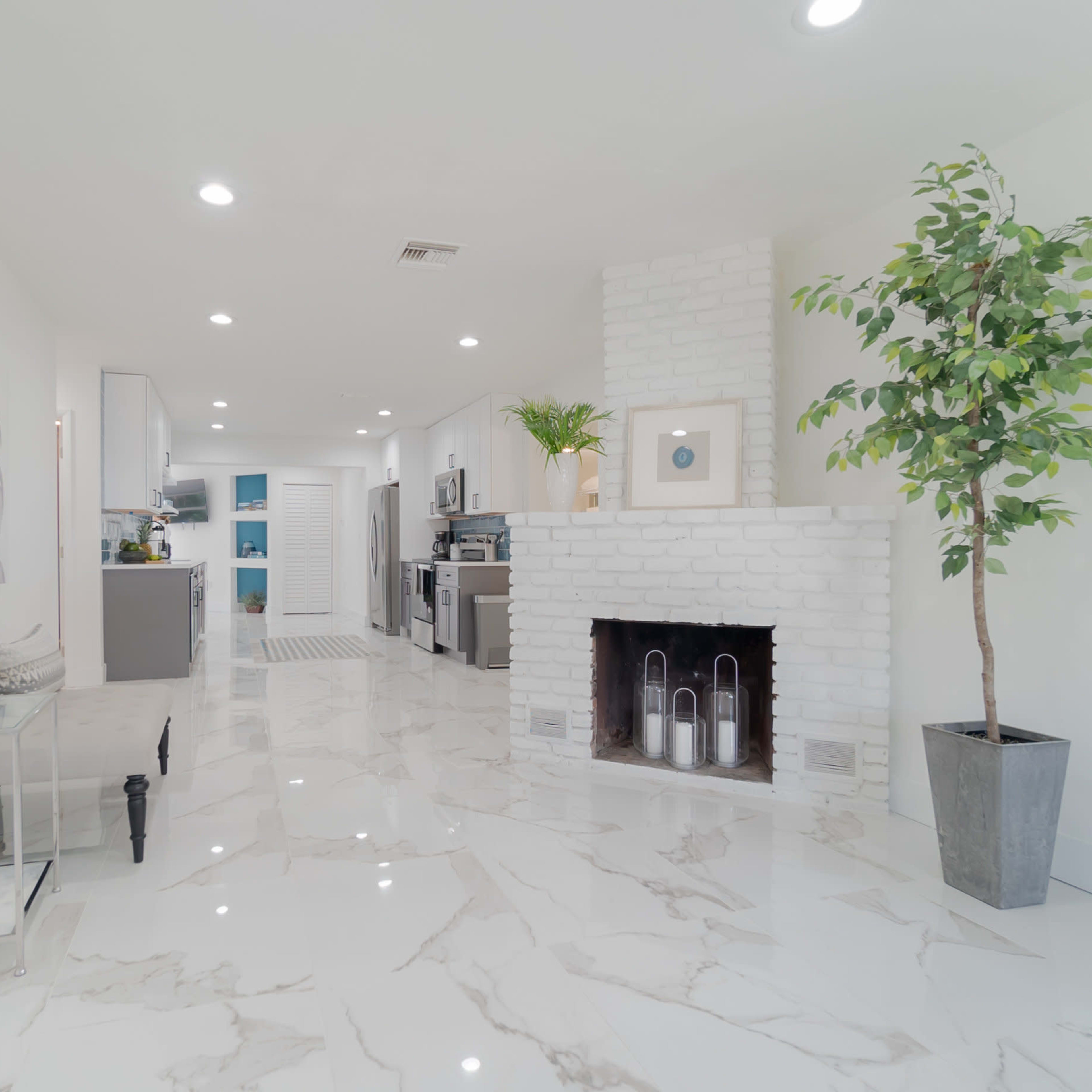 A modern, open-concept living space featuring a white brick fireplace, glossy marble floors, and a kitchenette in the background.