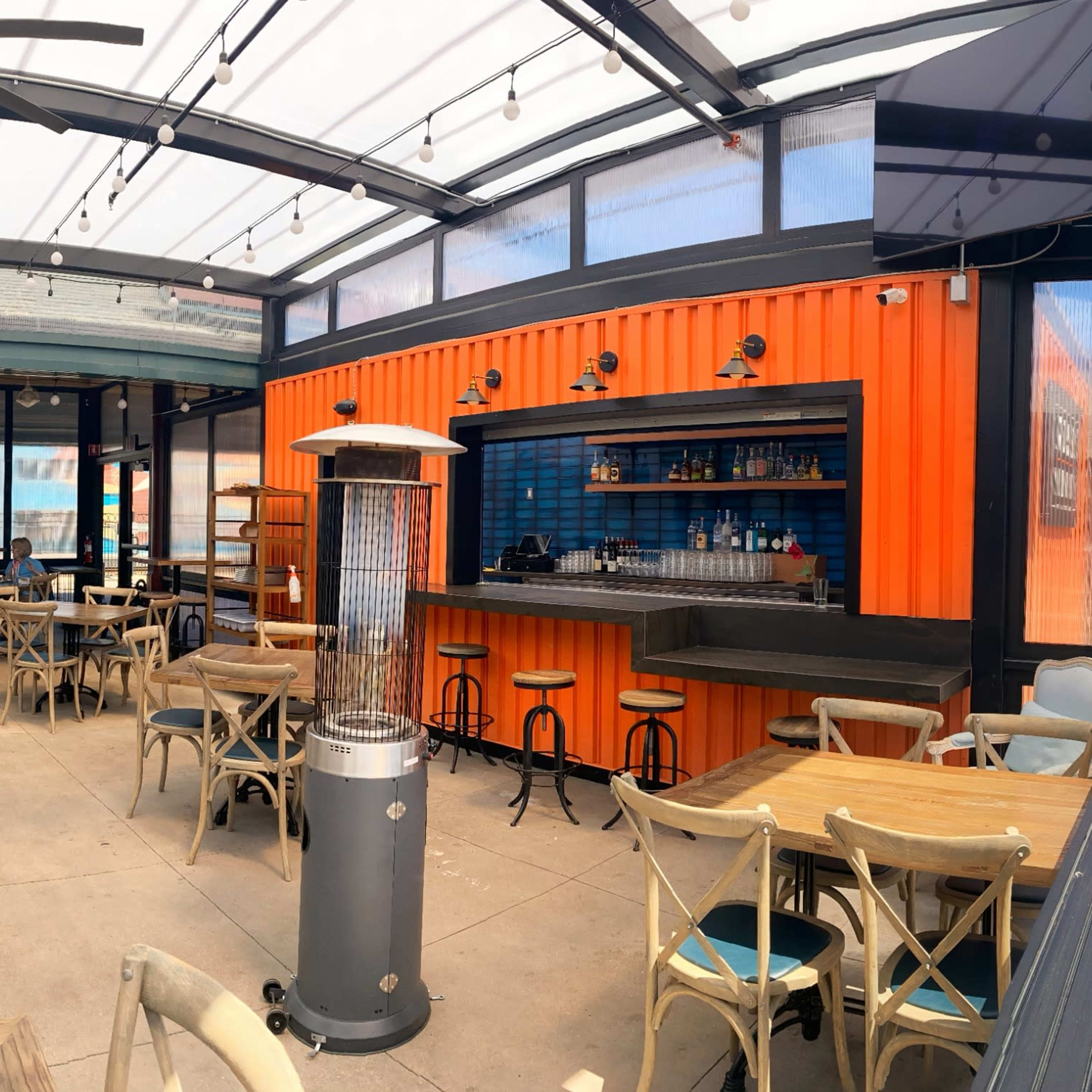 A spacious outdoor dining area with tables and chairs arranged neatly under a glass-roofed structure.
