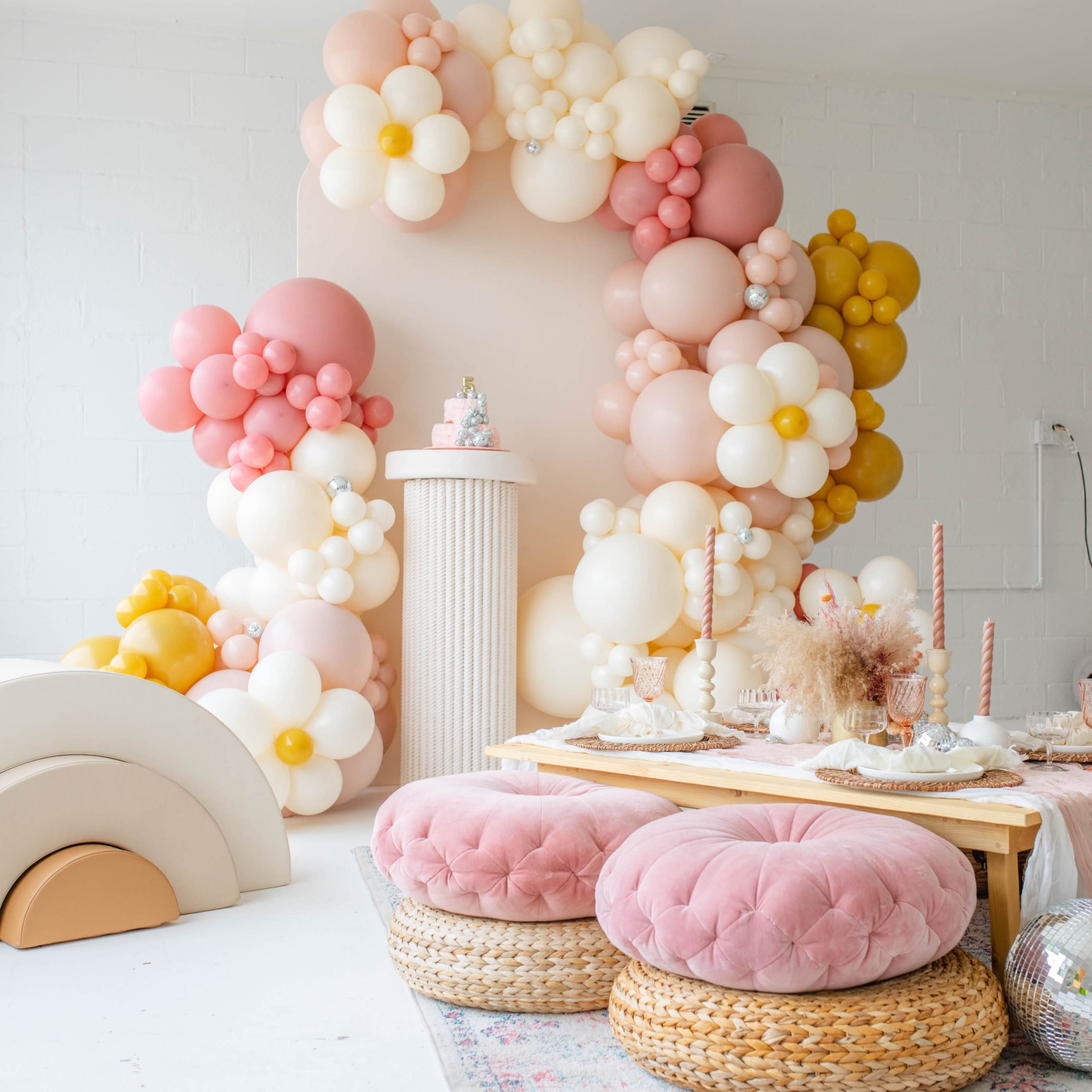 A decorated room featuring a table set with candles and desserts, surrounded by a colorful balloon backdrop and plush seating.