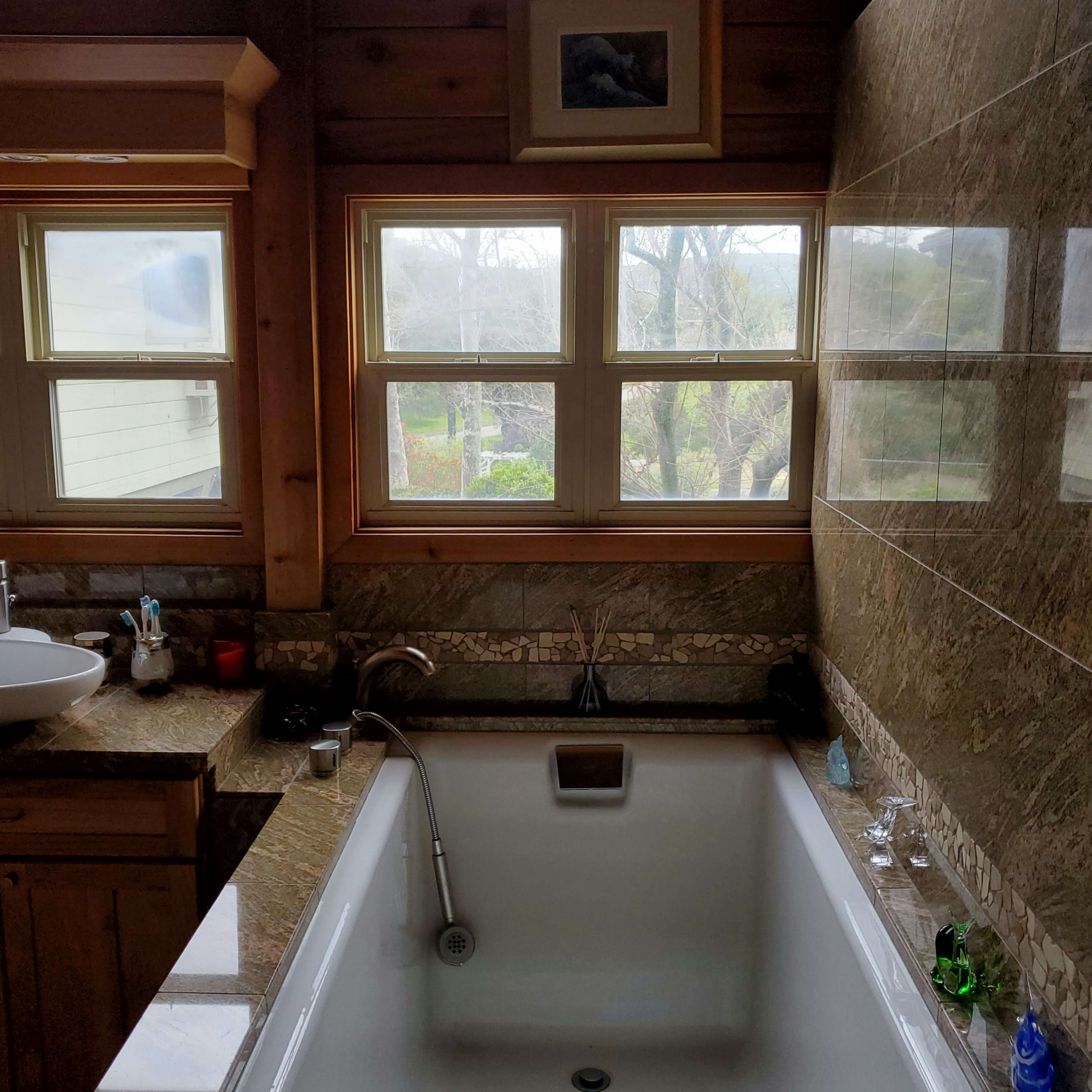 A modern bathroom features a white bathtub alongside a stone countertop and large windows offering a view of the outdoors.