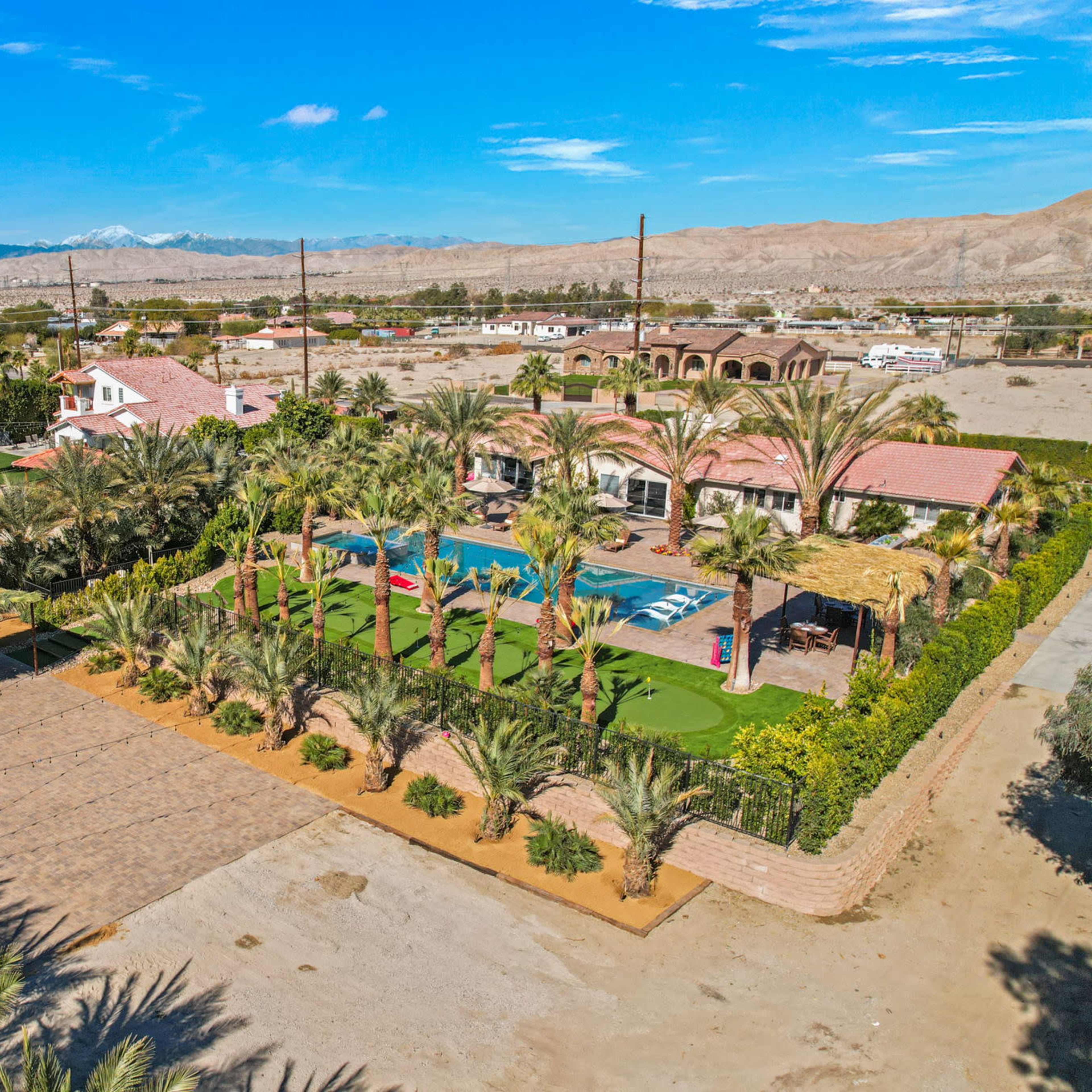 A resort-like setting featuring a swimming pool, palm trees, and landscaped areas surrounded by residential buildings and mountains in the background.