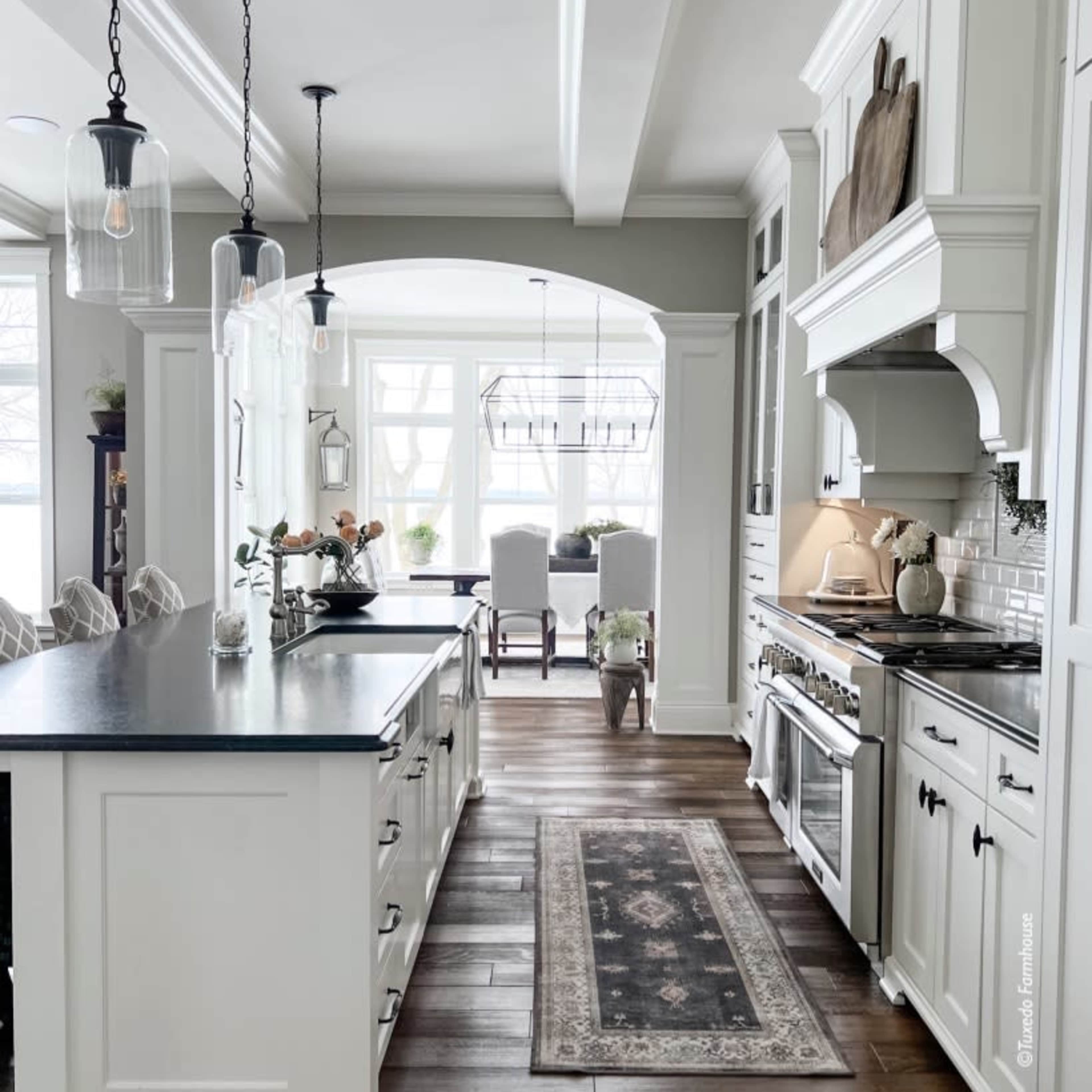 A modern kitchen with a central island, pendant lighting, and a dining area visible through an archway.