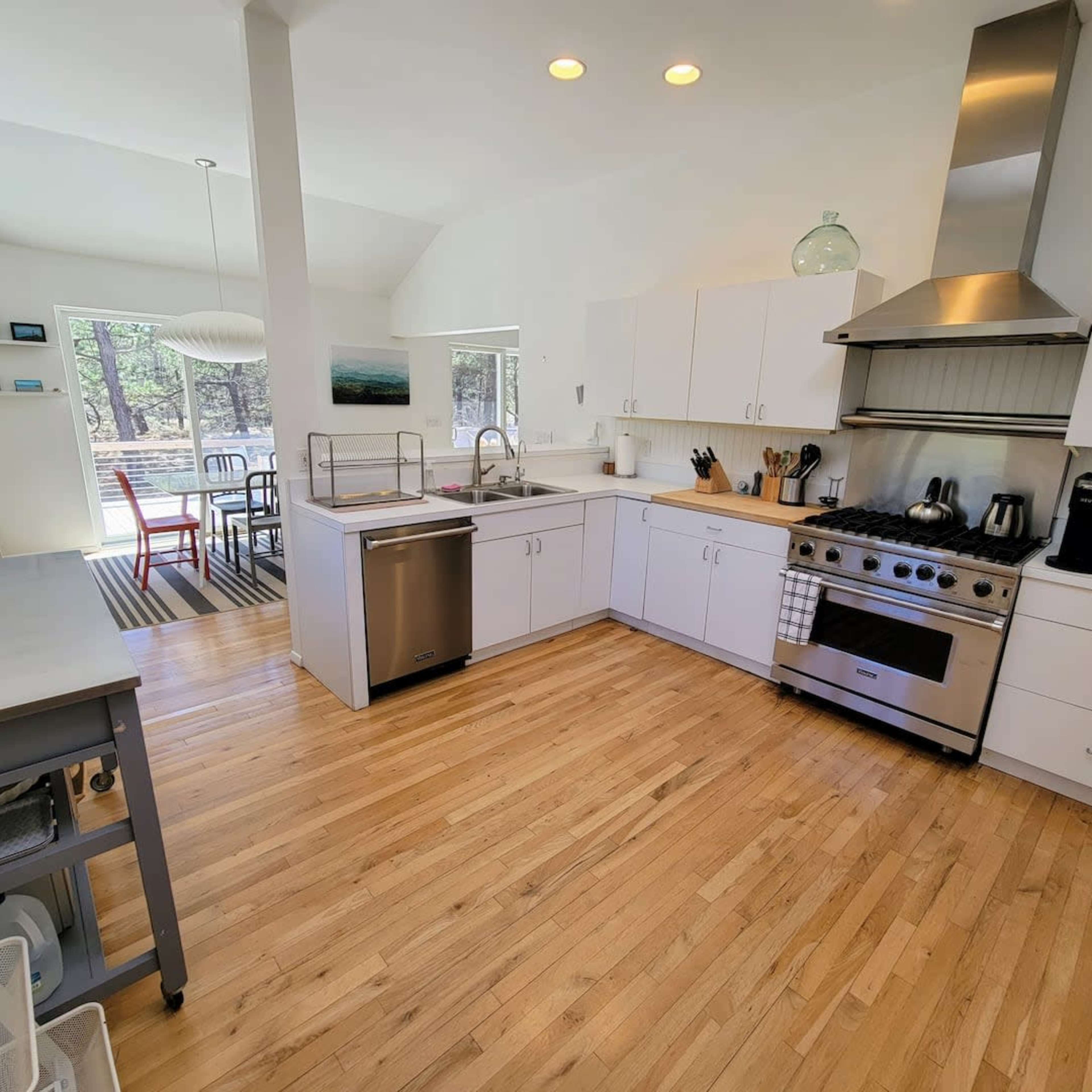A modern kitchen with white cabinetry, a large stove, stainless steel appliances, and wooden flooring.