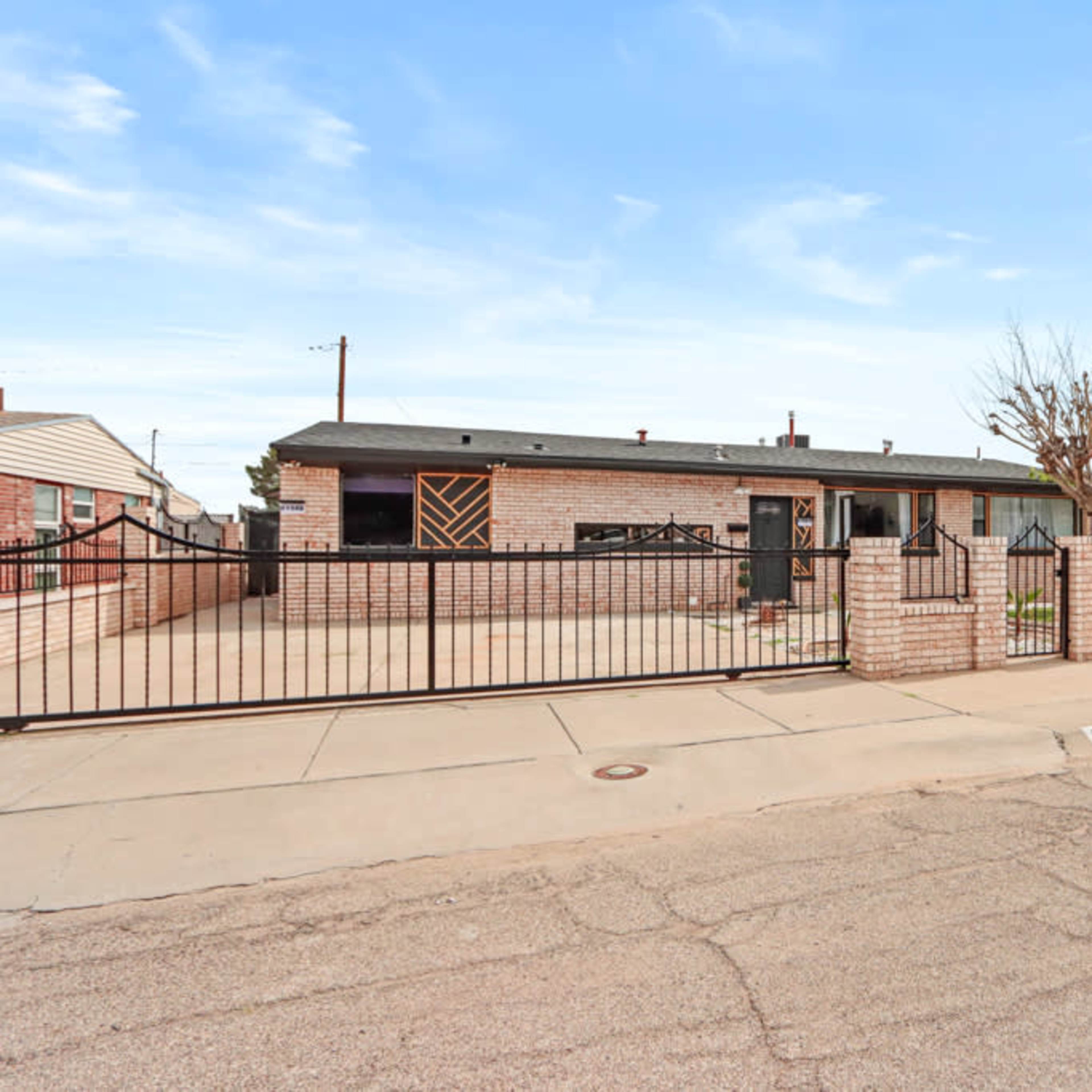 A single-story brick house with a fenced yard and a concrete driveway is situated along a residential street.