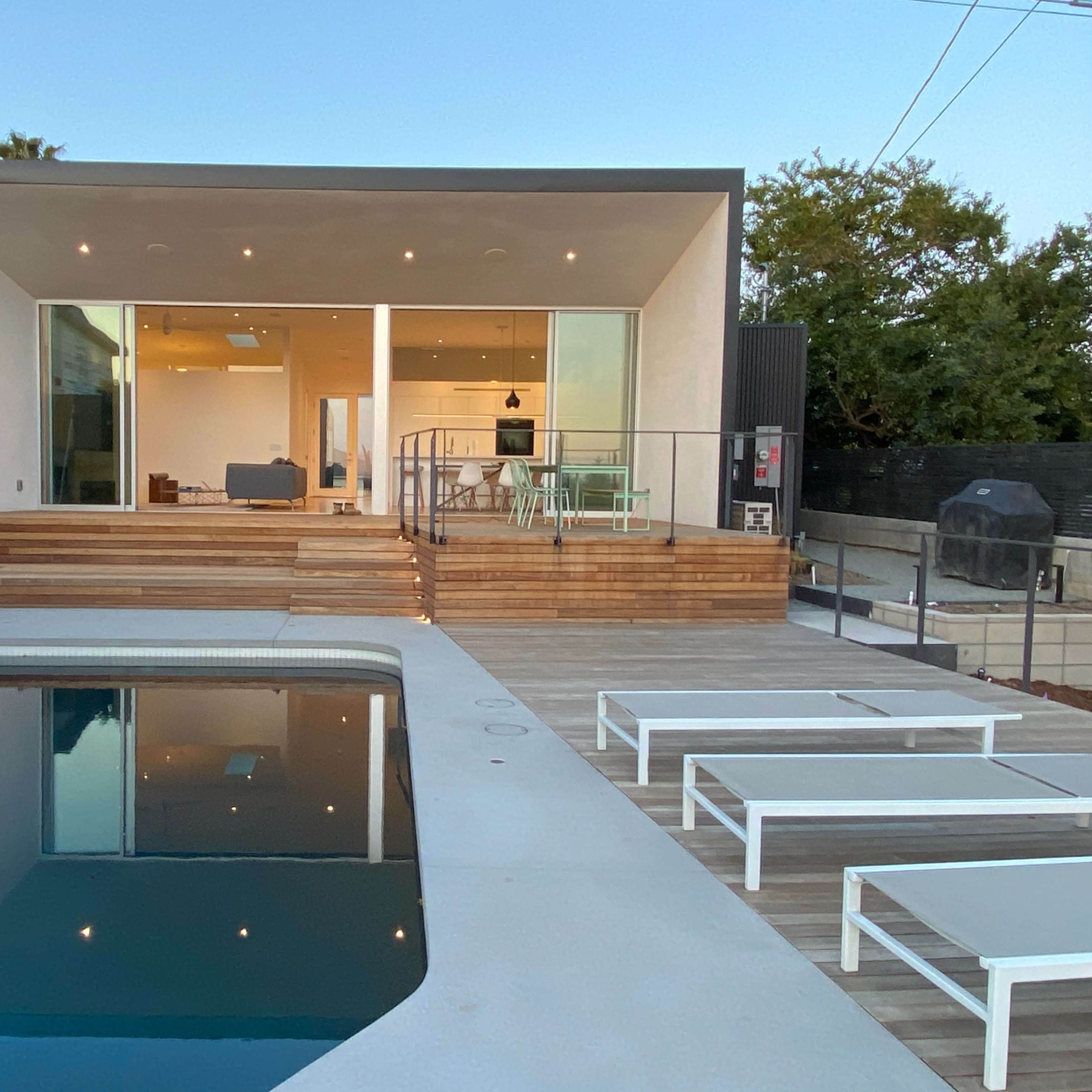 A modern house with large windows features a wooden deck and a swimming pool in the foreground.