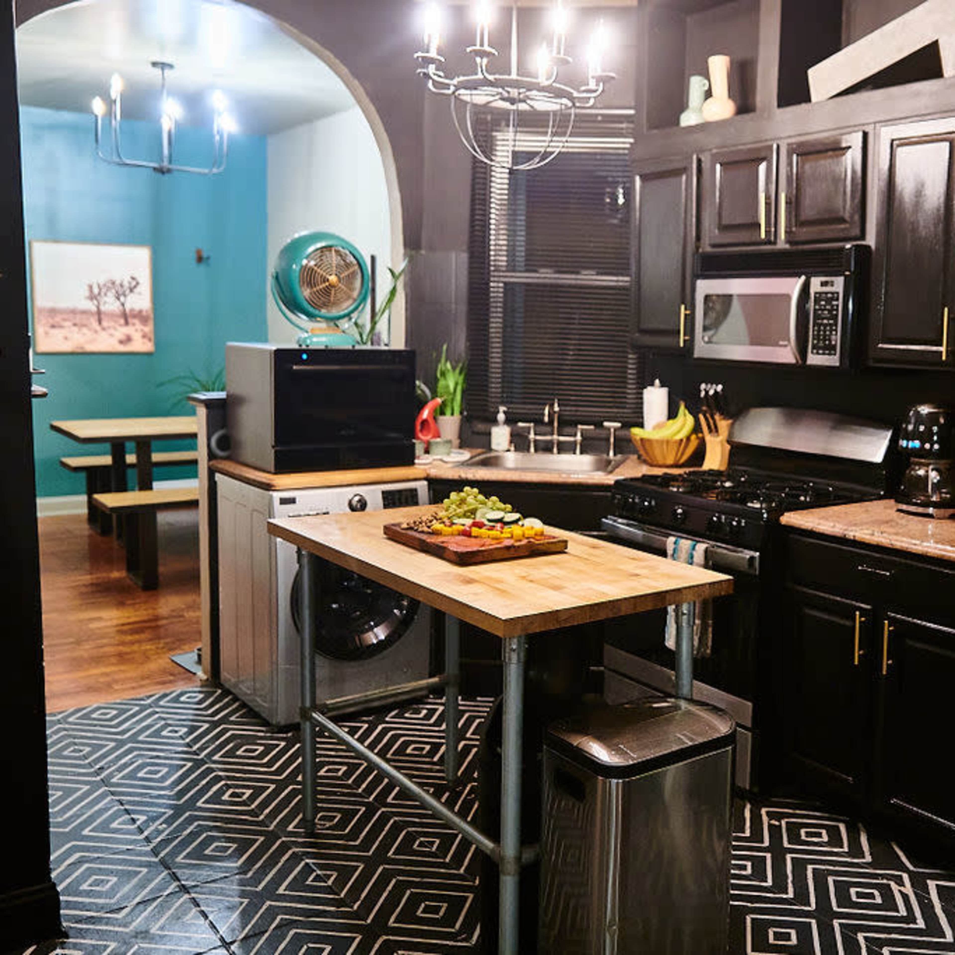 A modern kitchen features black cabinetry, stainless steel appliances, and a wooden kitchen island with a cutting board and fresh vegetables.