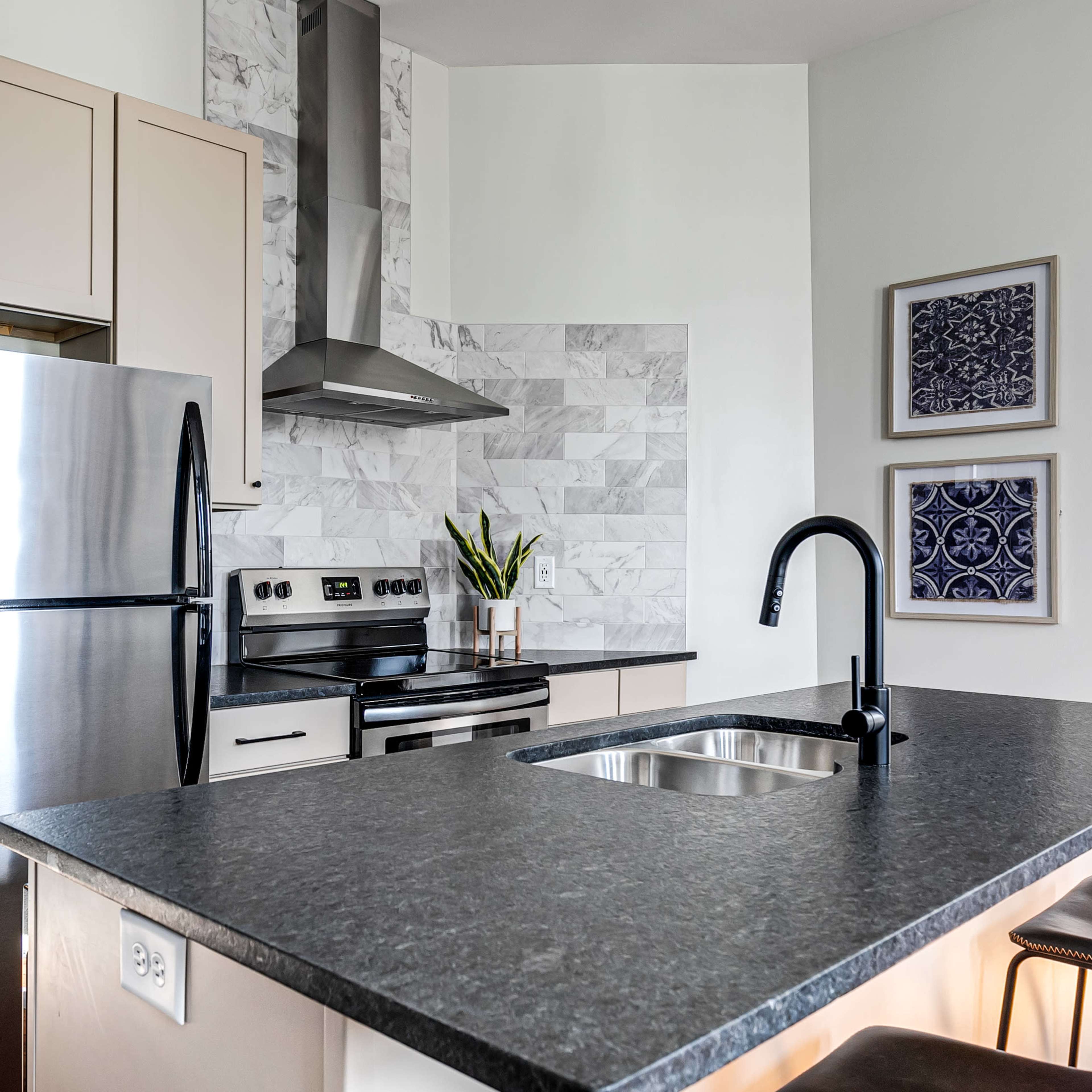 A modern kitchen featuring stainless steel appliances, a marble backsplash, and a dark countertop with a sink.
