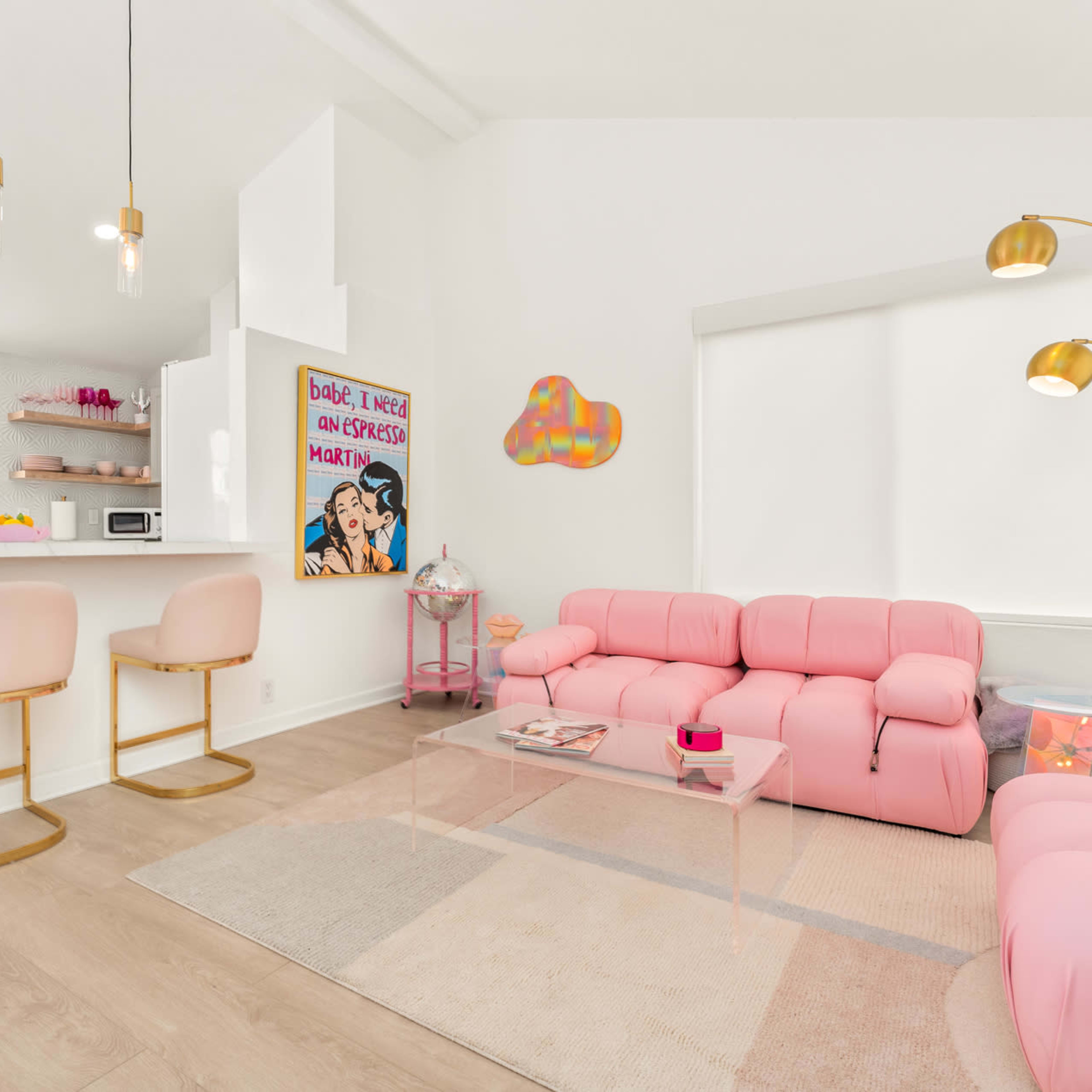 A bright living room features a pink sectional sofa, a glass coffee table, and a bar area with two stools.
