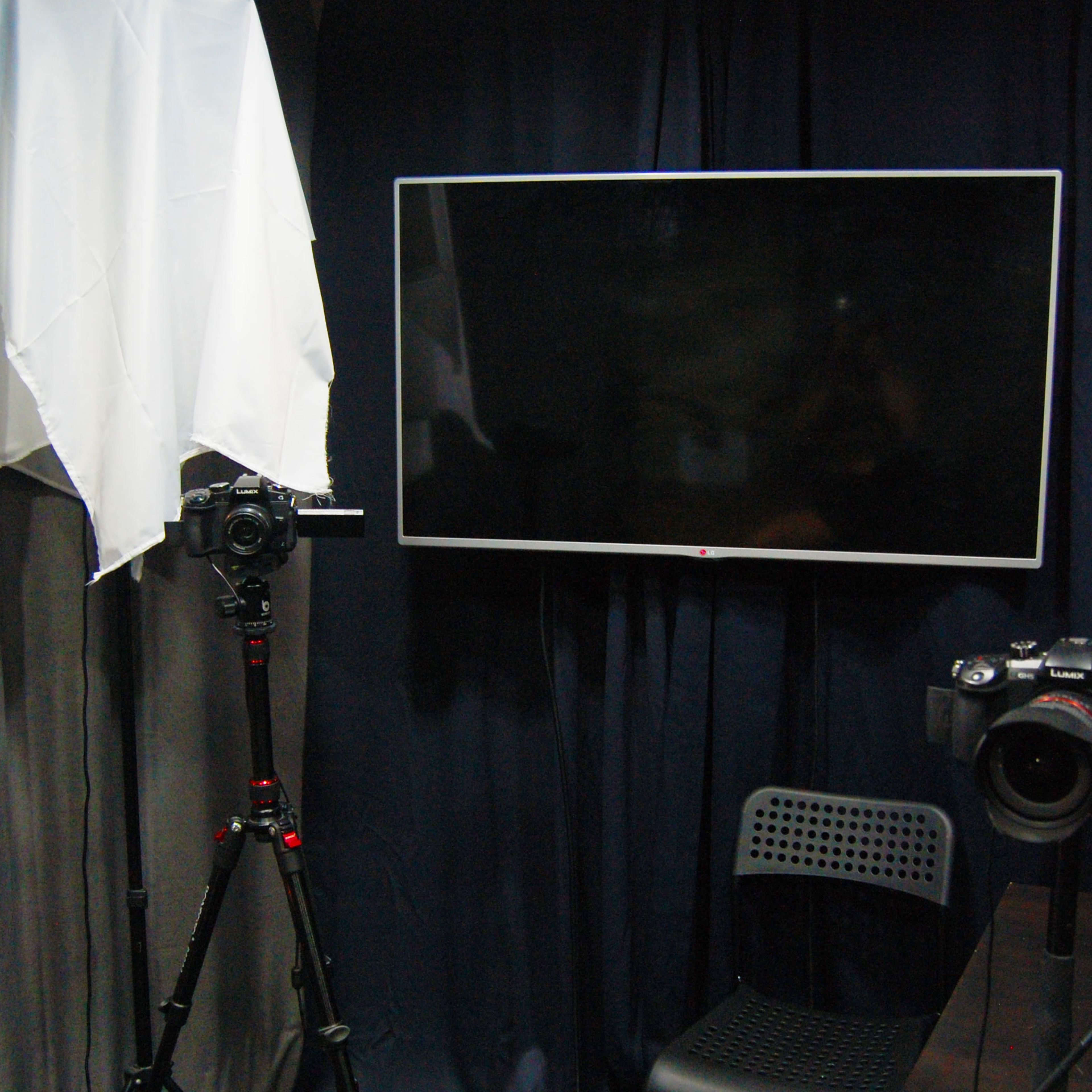 A photography setup with a camera on a tripod, a large television screen, and a second camera positioned on a table.