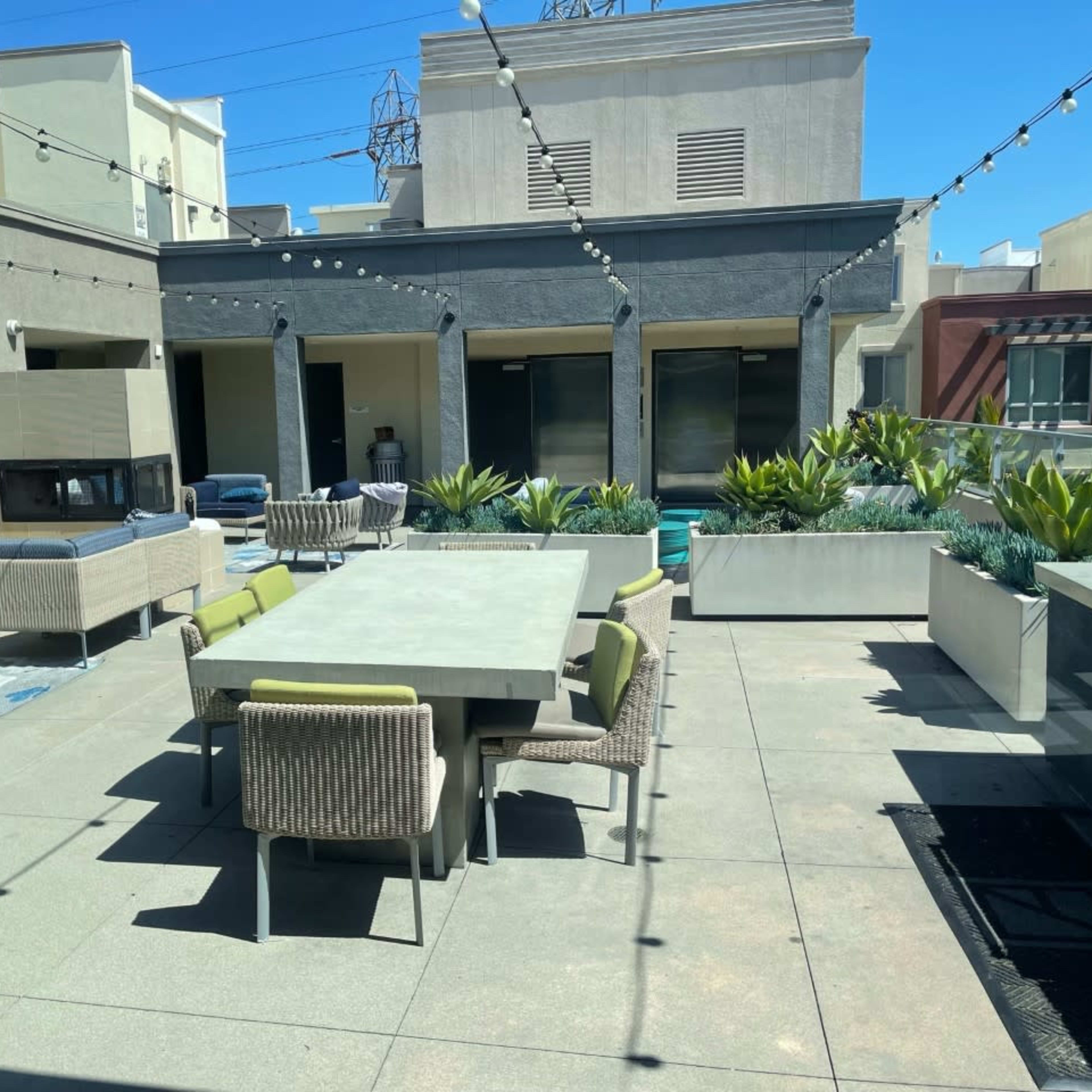 A modern rooftop terrace featuring a large dining table surrounded by various seating areas and planters.