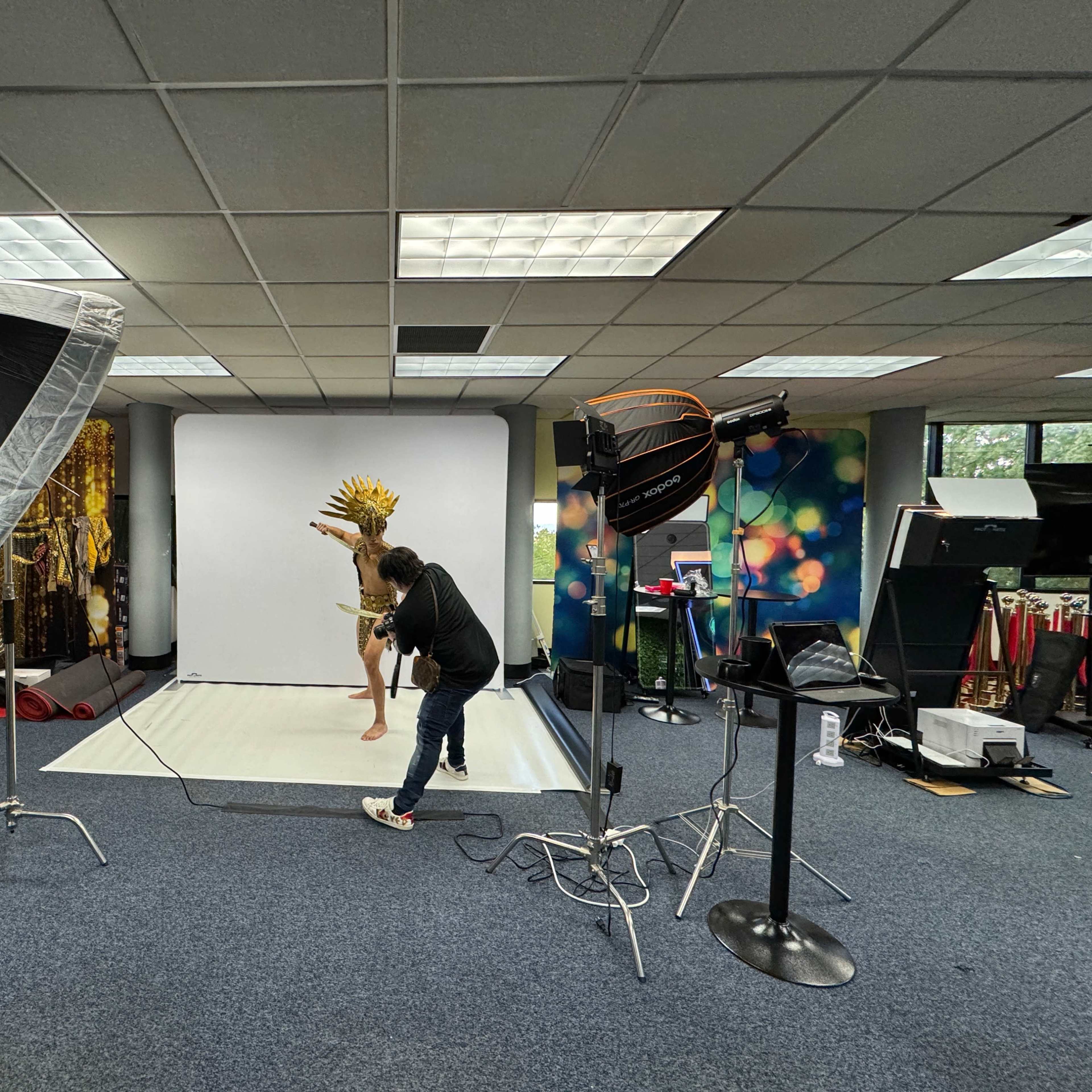 A photographer captures an image of a model posing with a headdress in a studio setting equipped with multiple lighting setups.
