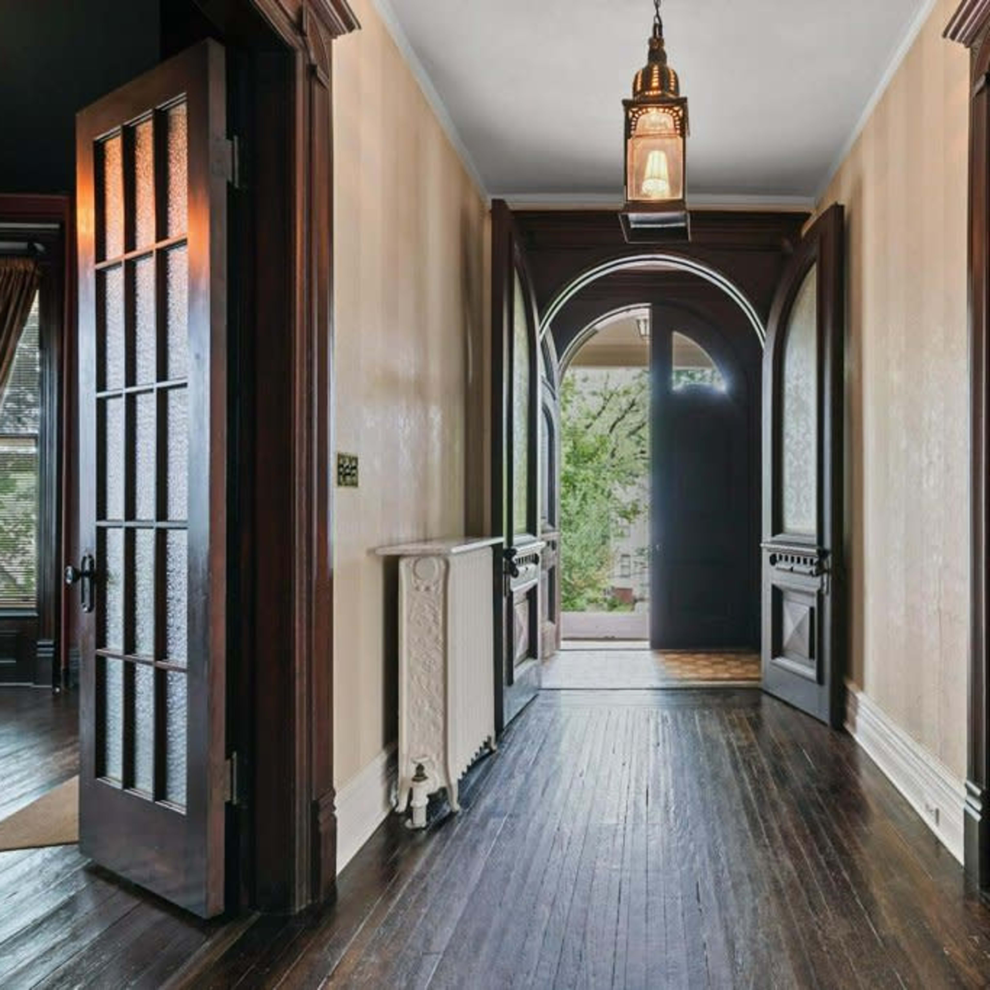 A hallway with arched doorways and wooden floors, featuring doorways leading to adjacent rooms and a lantern hanging from the ceiling.