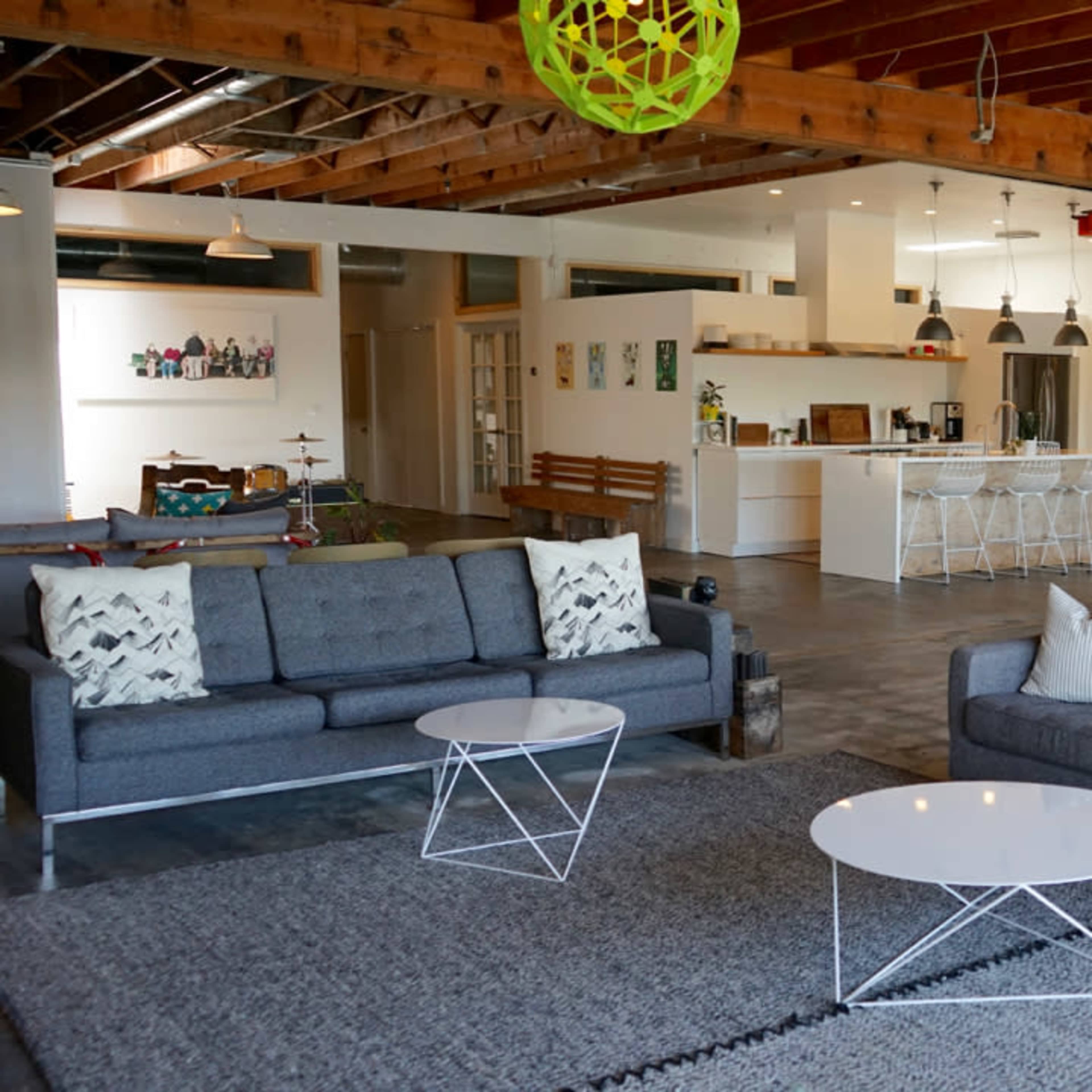 A spacious, modern open-concept living area featuring gray sofas, white tables, and a kitchen in the background.