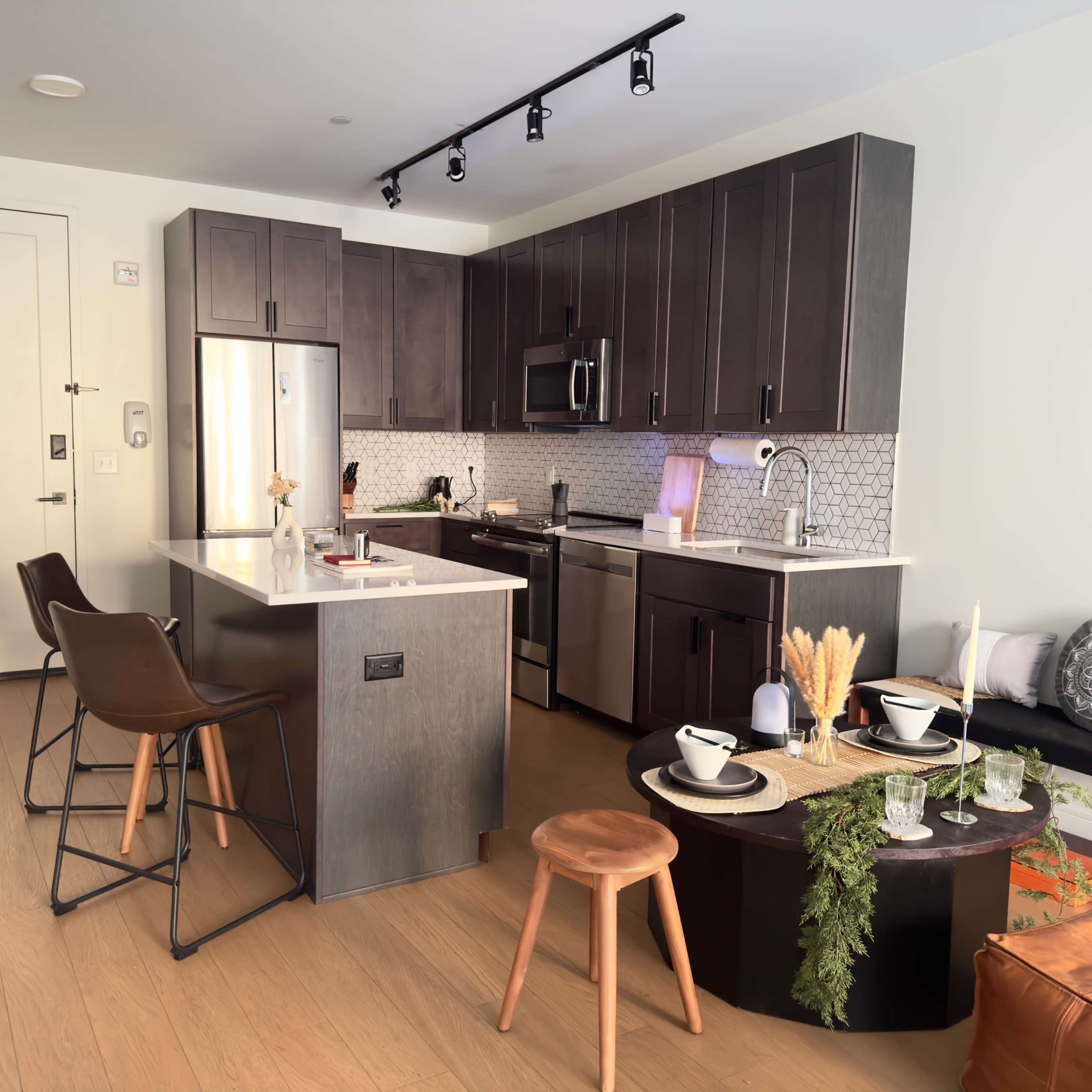 A modern kitchen with dark wood cabinets, stainless steel appliances, a central island with bar stools, and a dining table set with dishware and decorative items.