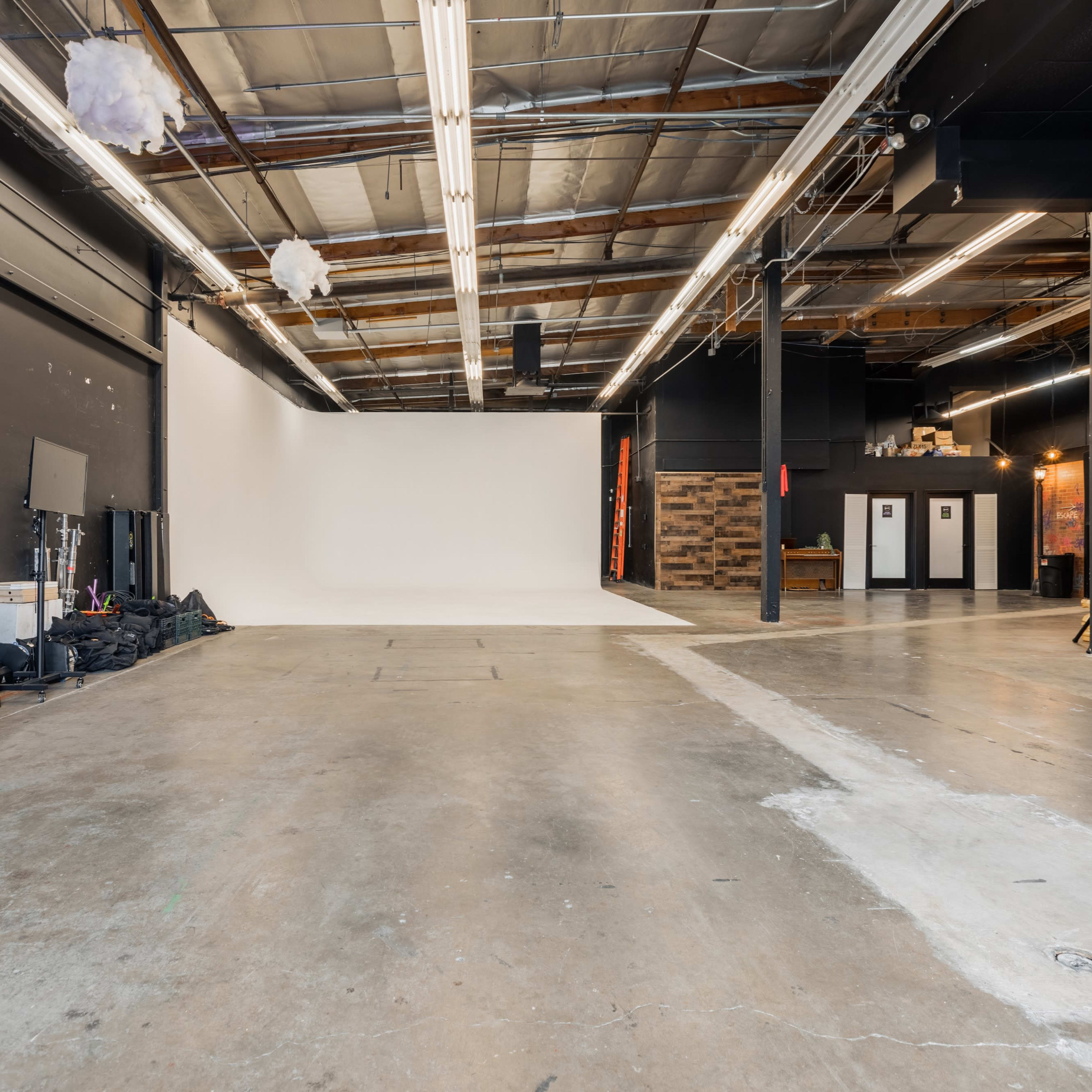 An industrial-style studio space with a white backdrop, concrete flooring, and various equipment and furnishings along the walls.