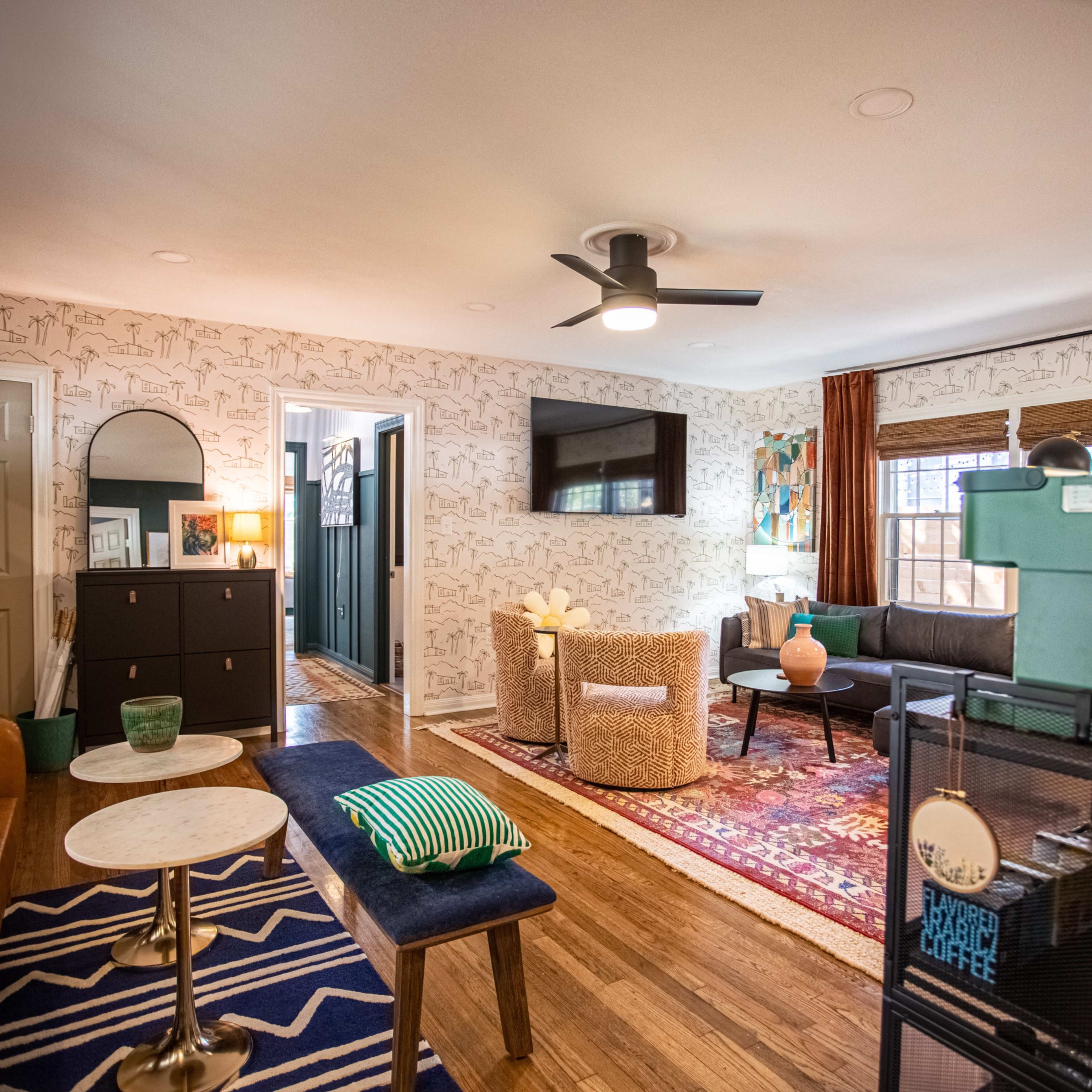 The living area features a mix of modern furniture, a patterned area rug, and decorative wall art.