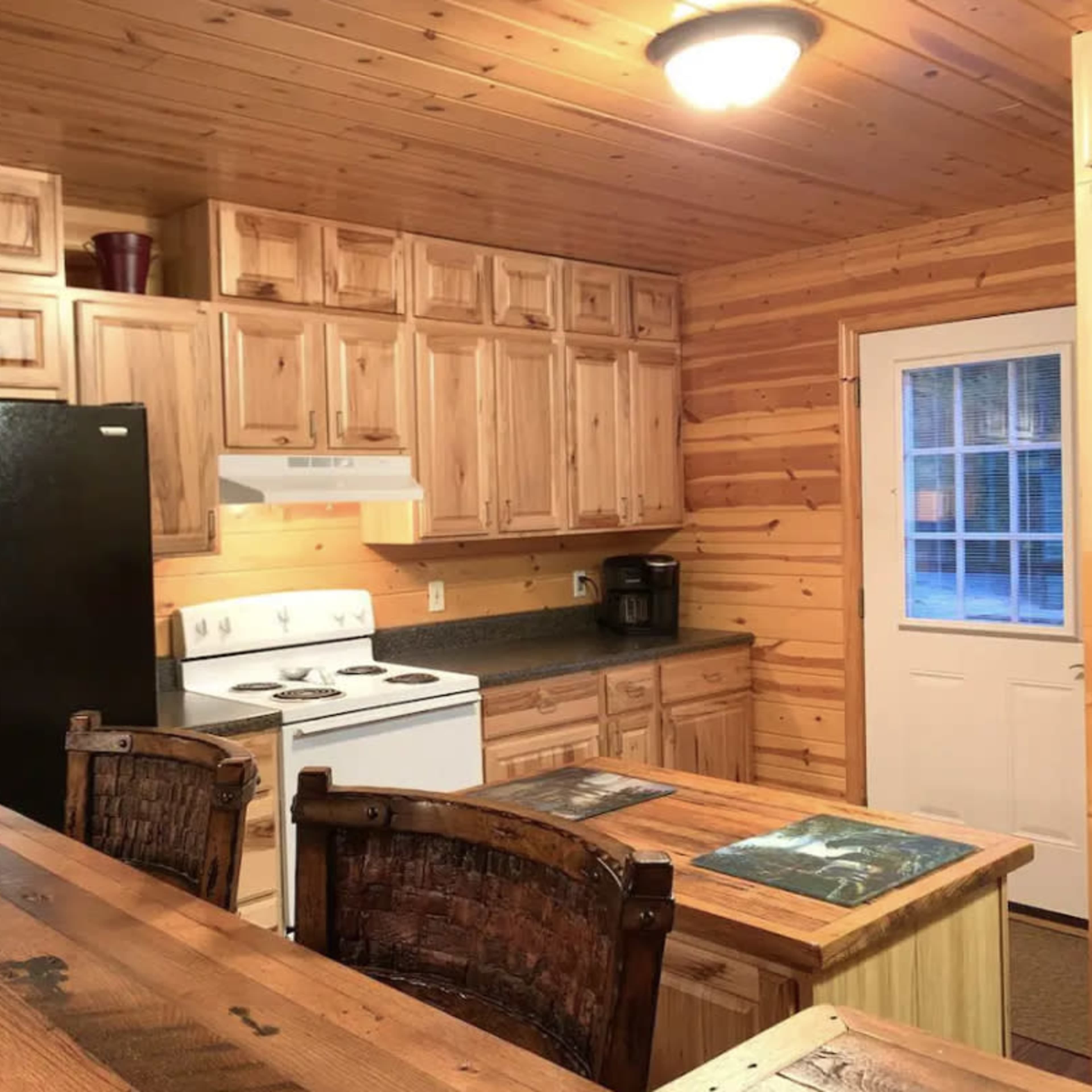A wooden cabin kitchen with a black refrigerator, white stove, and a wooden dining table surrounded by chairs.