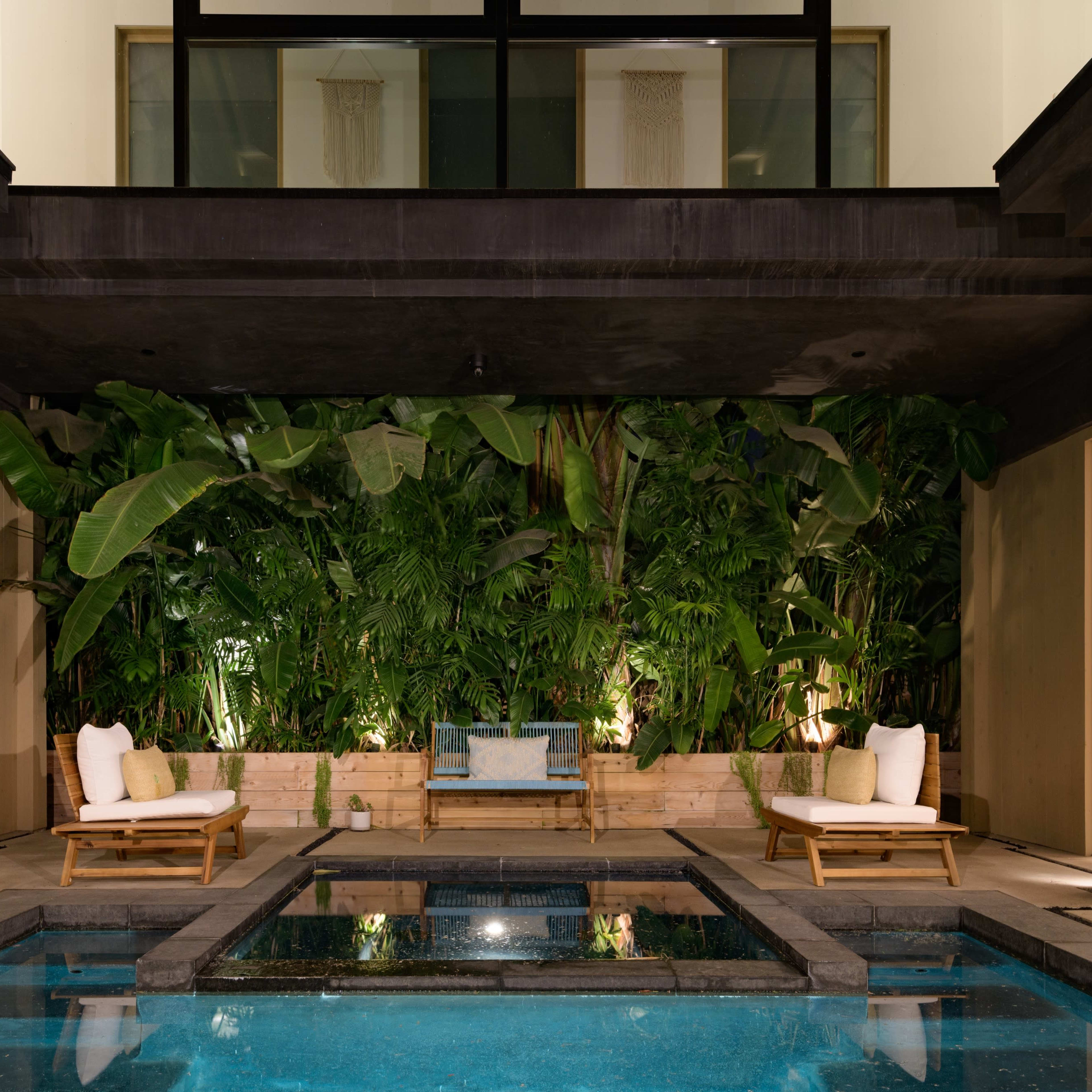 A modern indoor pool area surrounded by large tropical plants and seating.