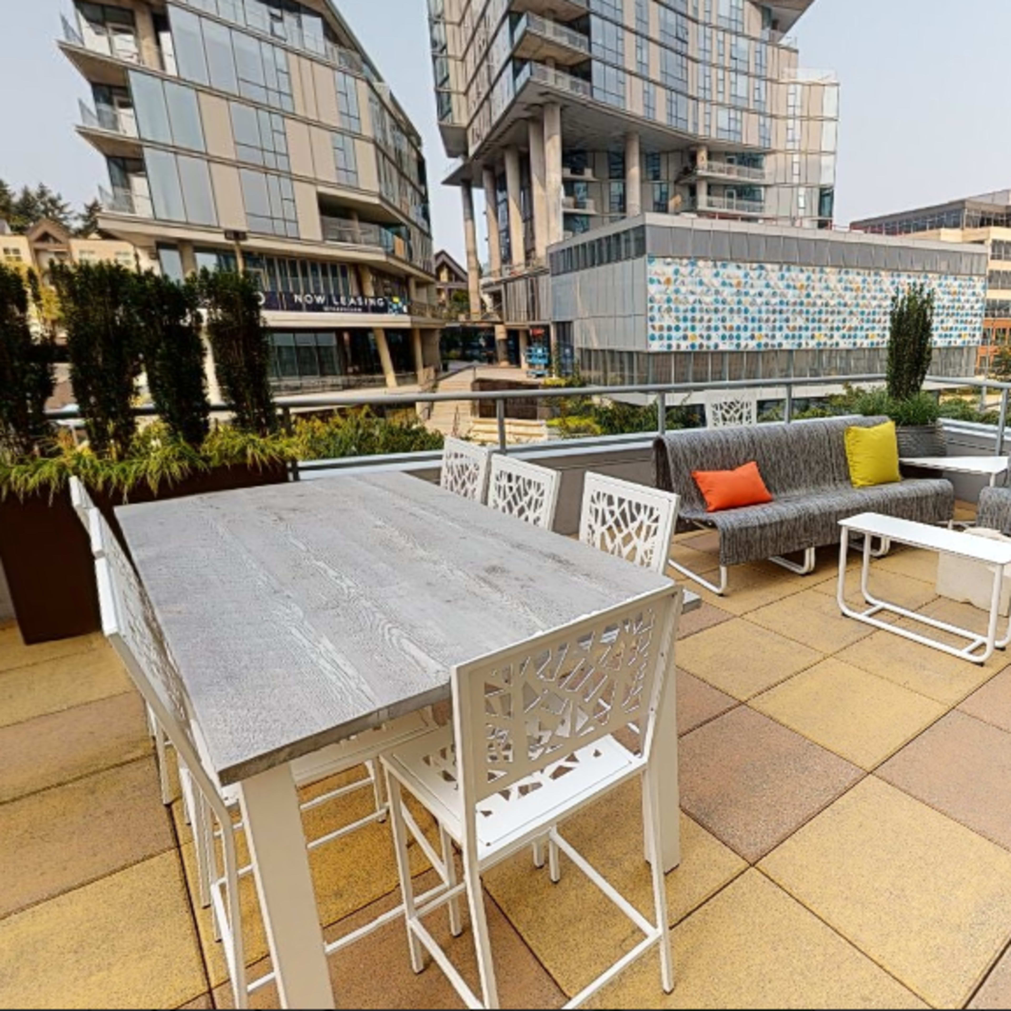 A modern rooftop patio featuring various seating areas and tables surrounded by buildings and greenery.