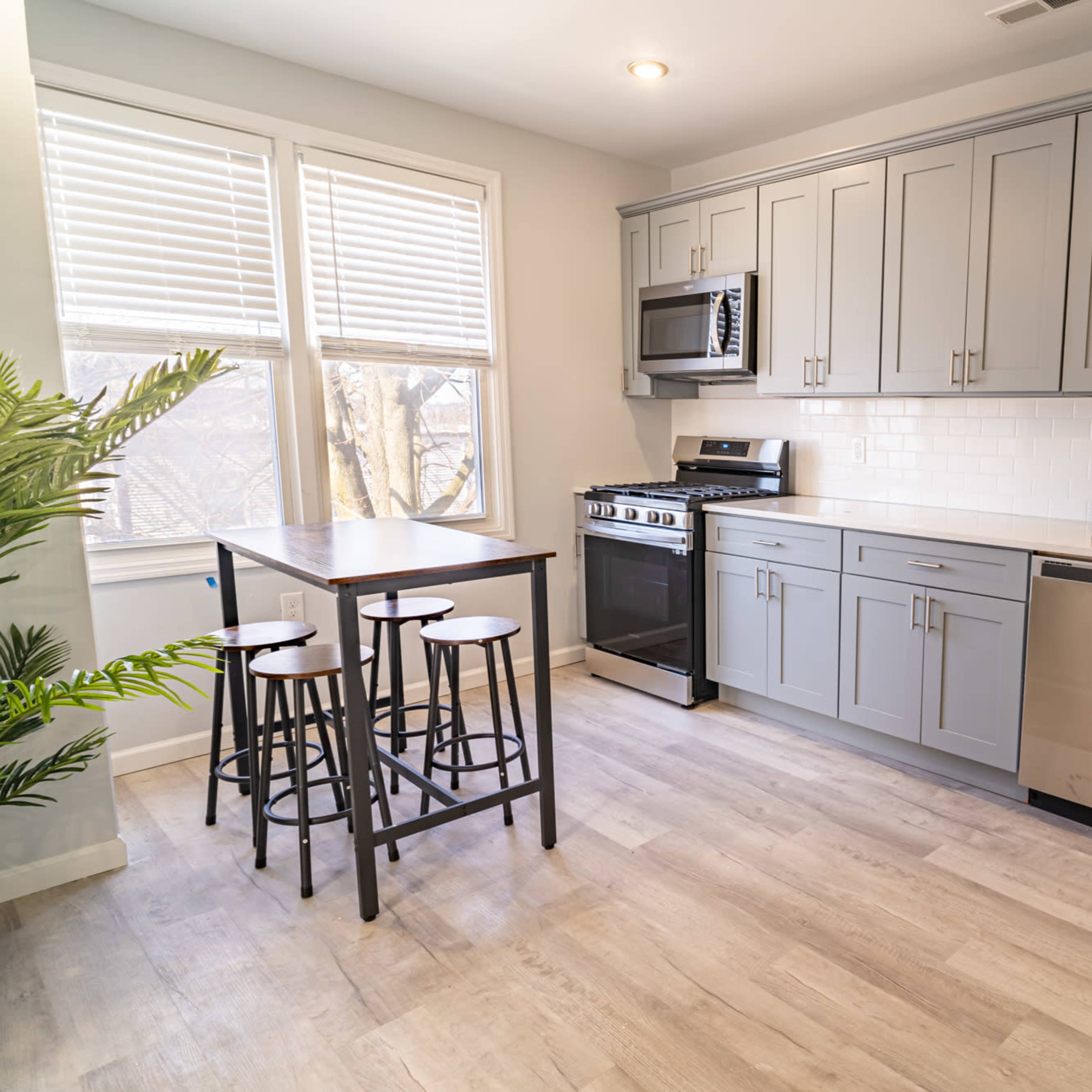 A modern kitchen with light gray cabinetry, stainless steel appliances, and a small dining table with four black stools.