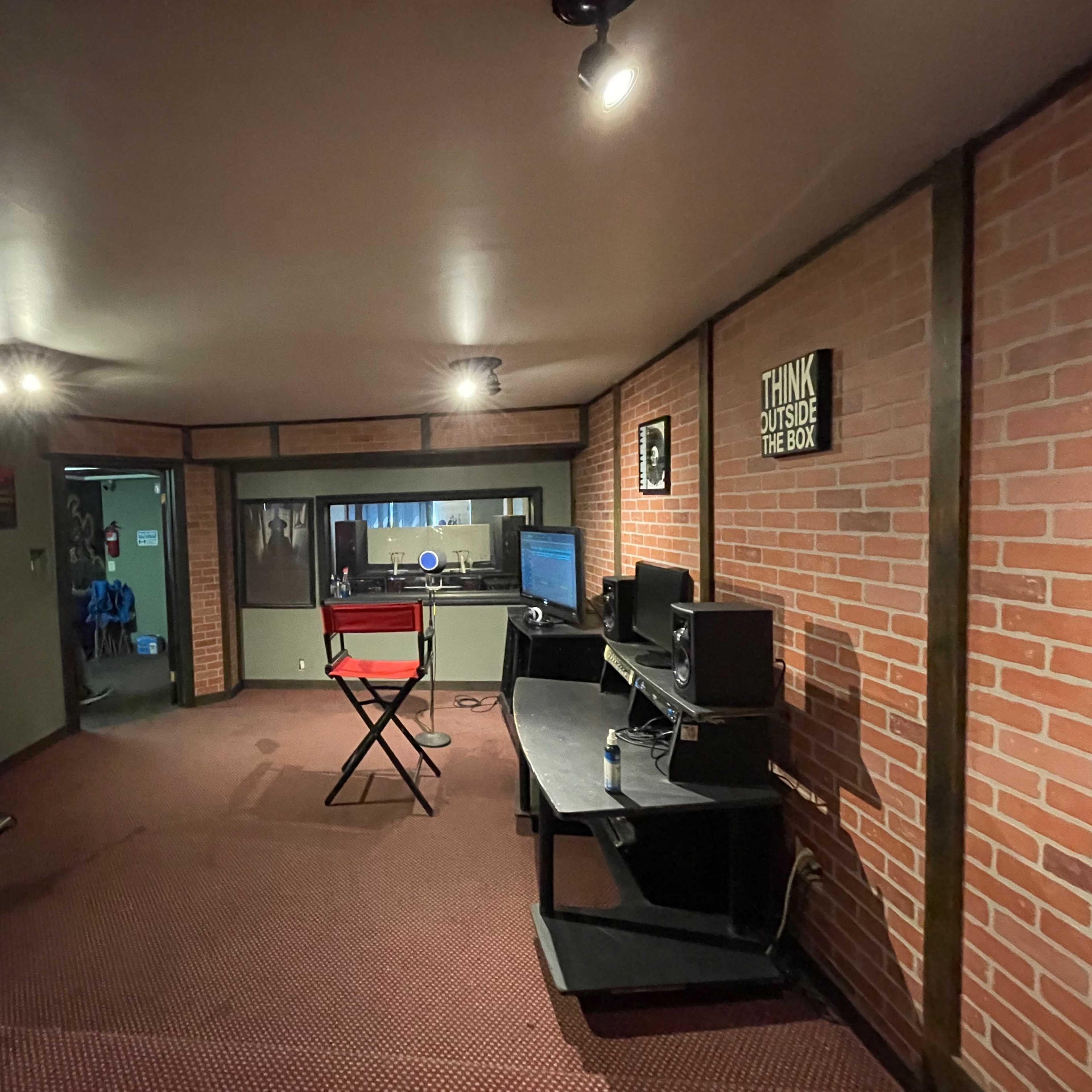 A music studio with brick walls, a black chair, a desk with a computer, and amplifiers in the corner.