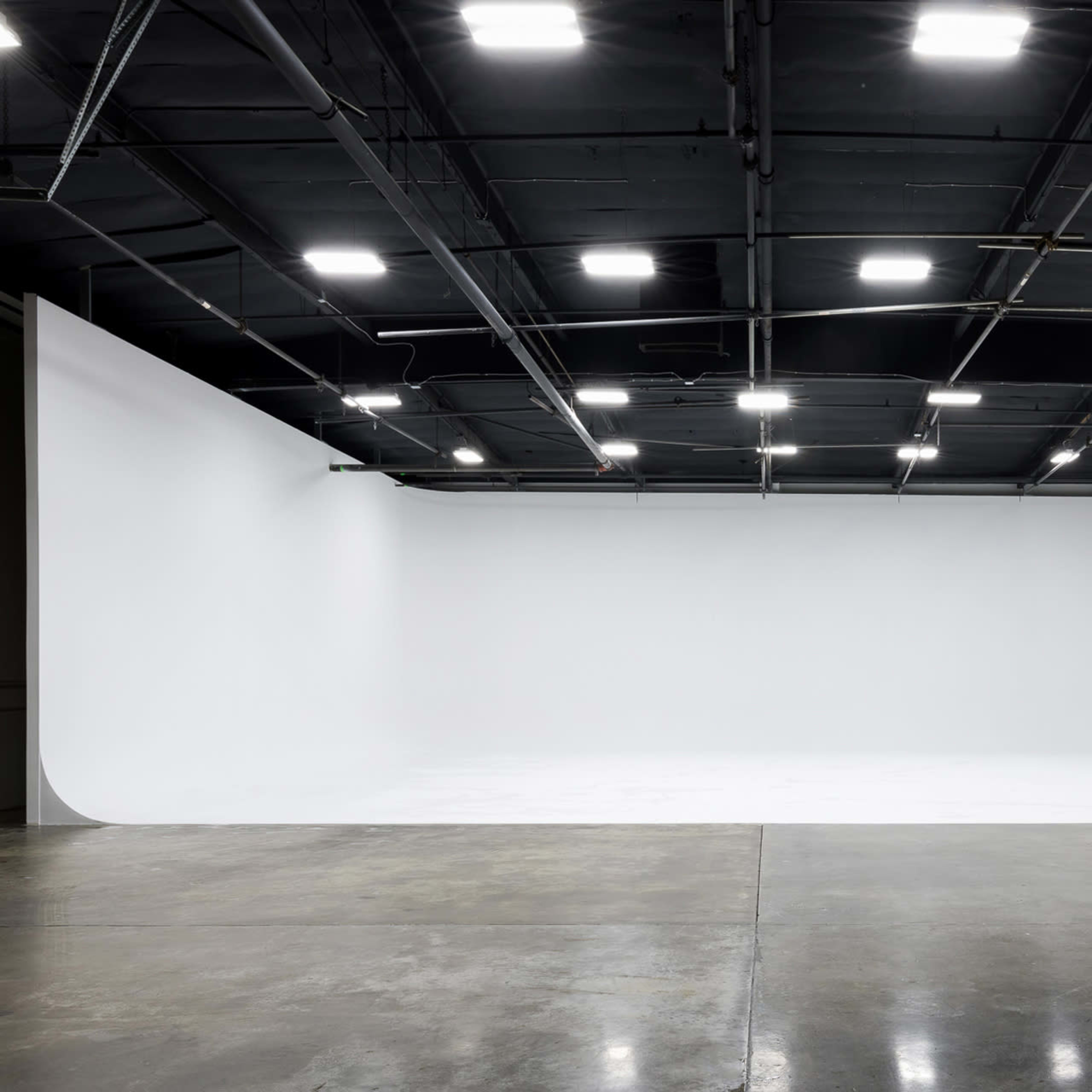 A large, empty studio space with a seamless white backdrop and overhead lighting.