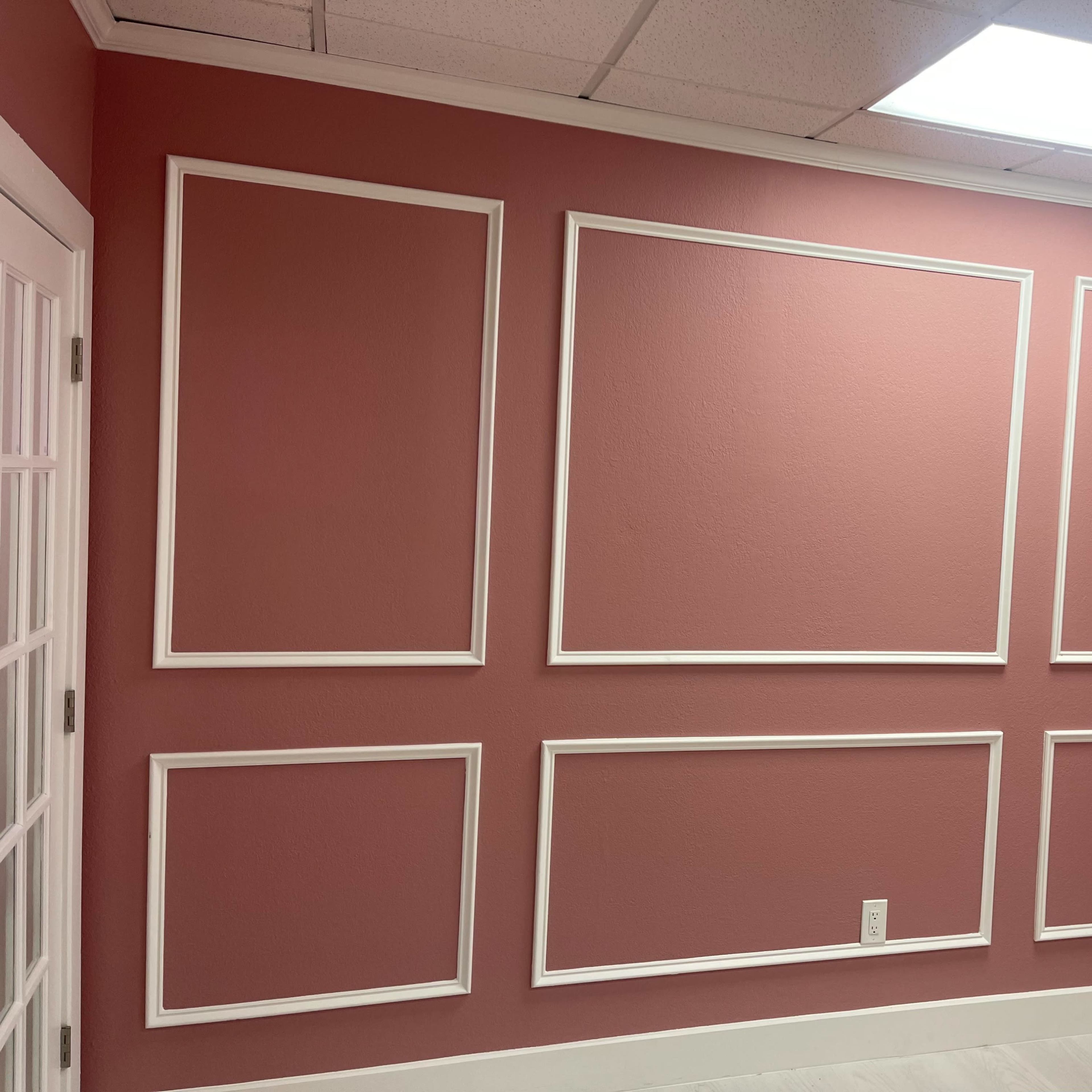 A pink wall featuring six white rectangular frames arranged in a grid pattern.