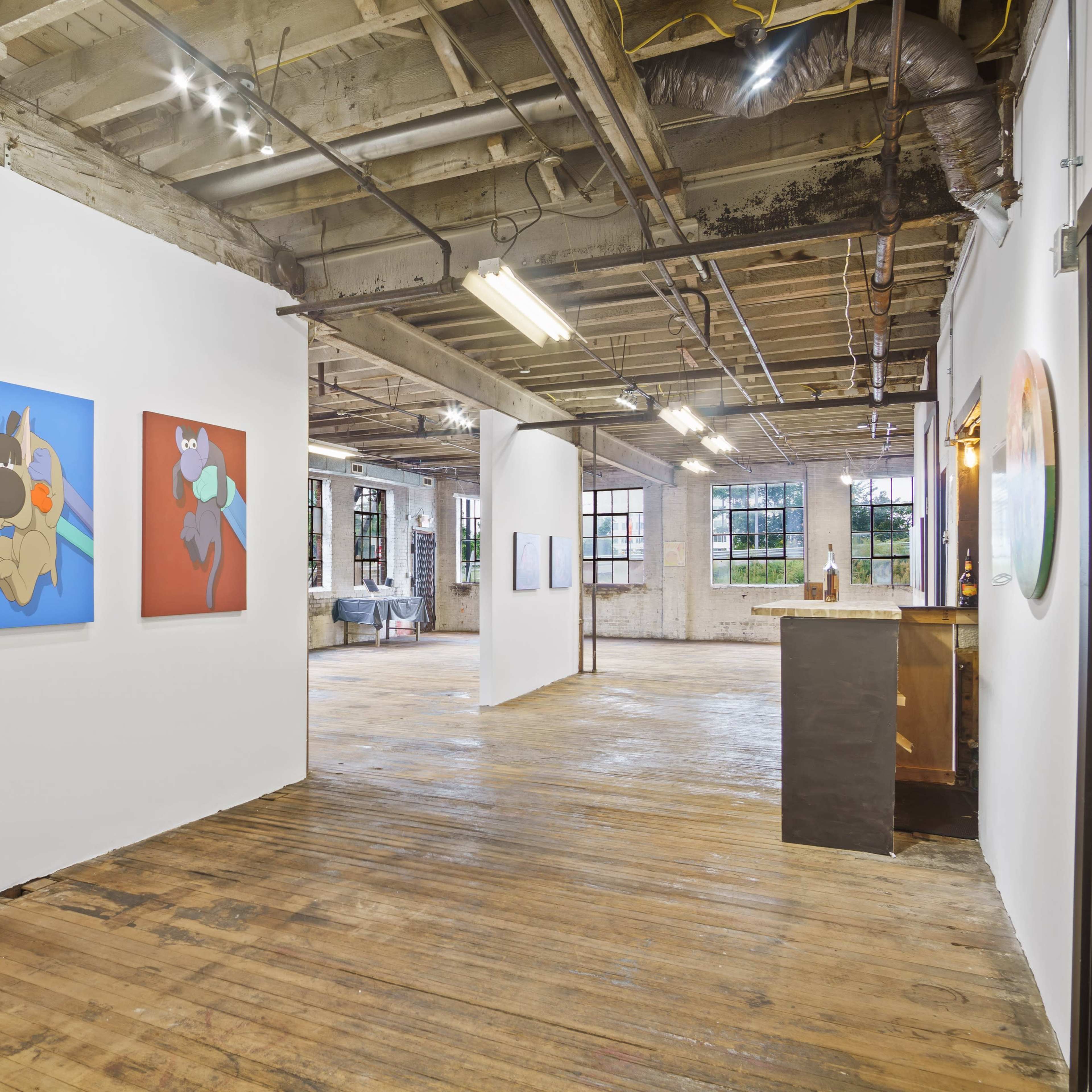 An art gallery featuring colorful paintings on the walls and a wooden floor in a spacious, well-lit interior.