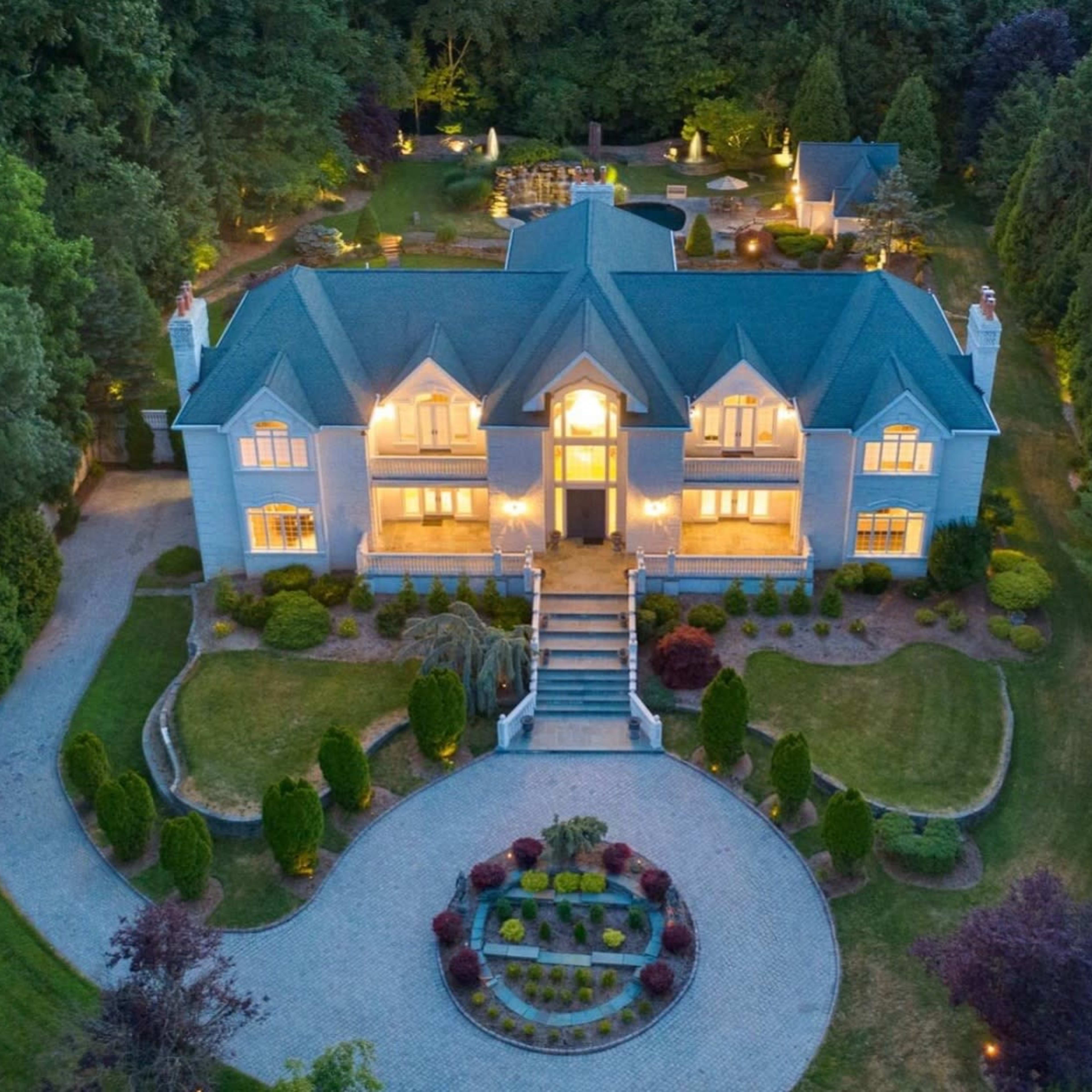 A large, elegant mansion with a green roof is surrounded by well-manicured gardens and a circular driveway.