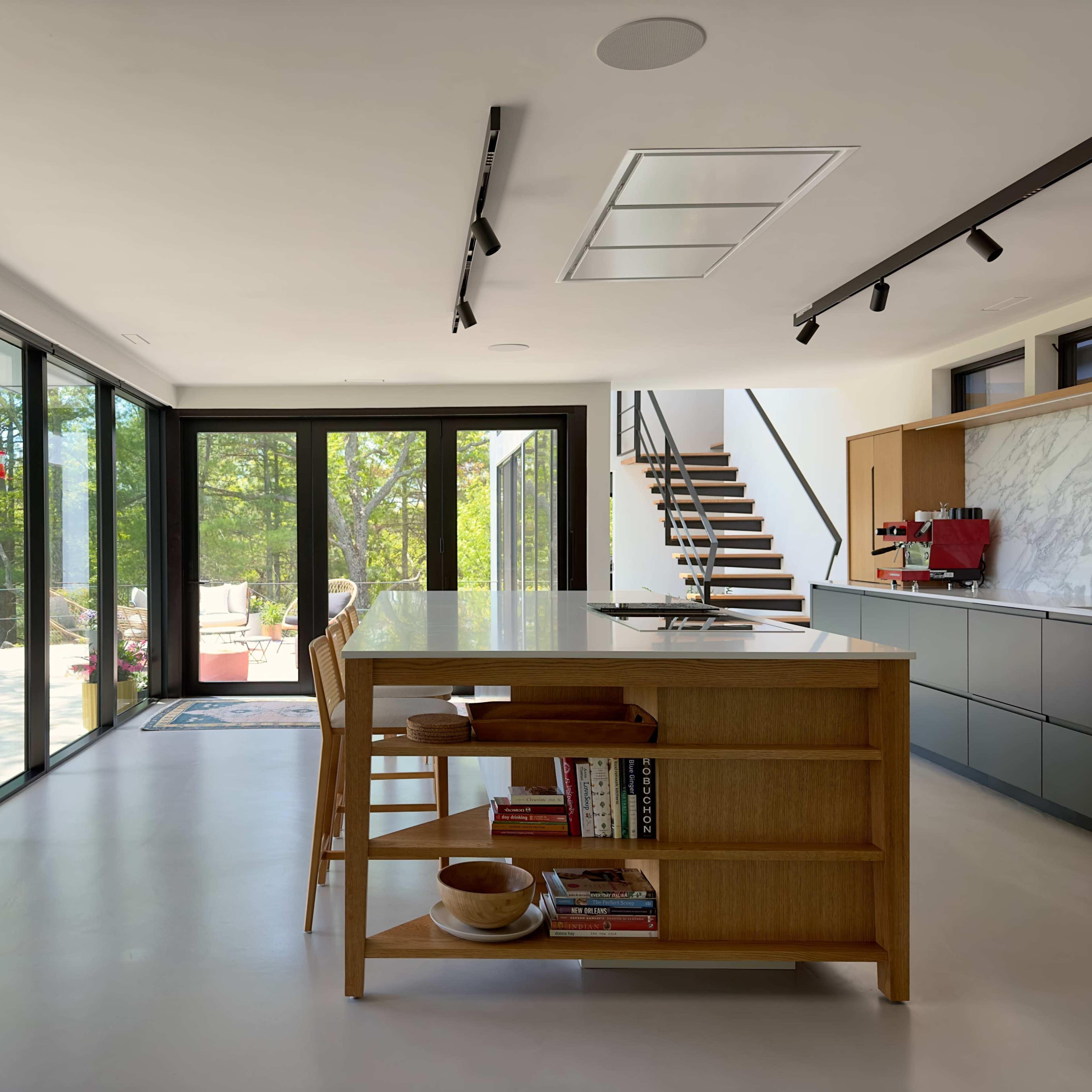 A modern living space with a seating area featuring large windows overlooking a green landscape and a dining table with chairs.