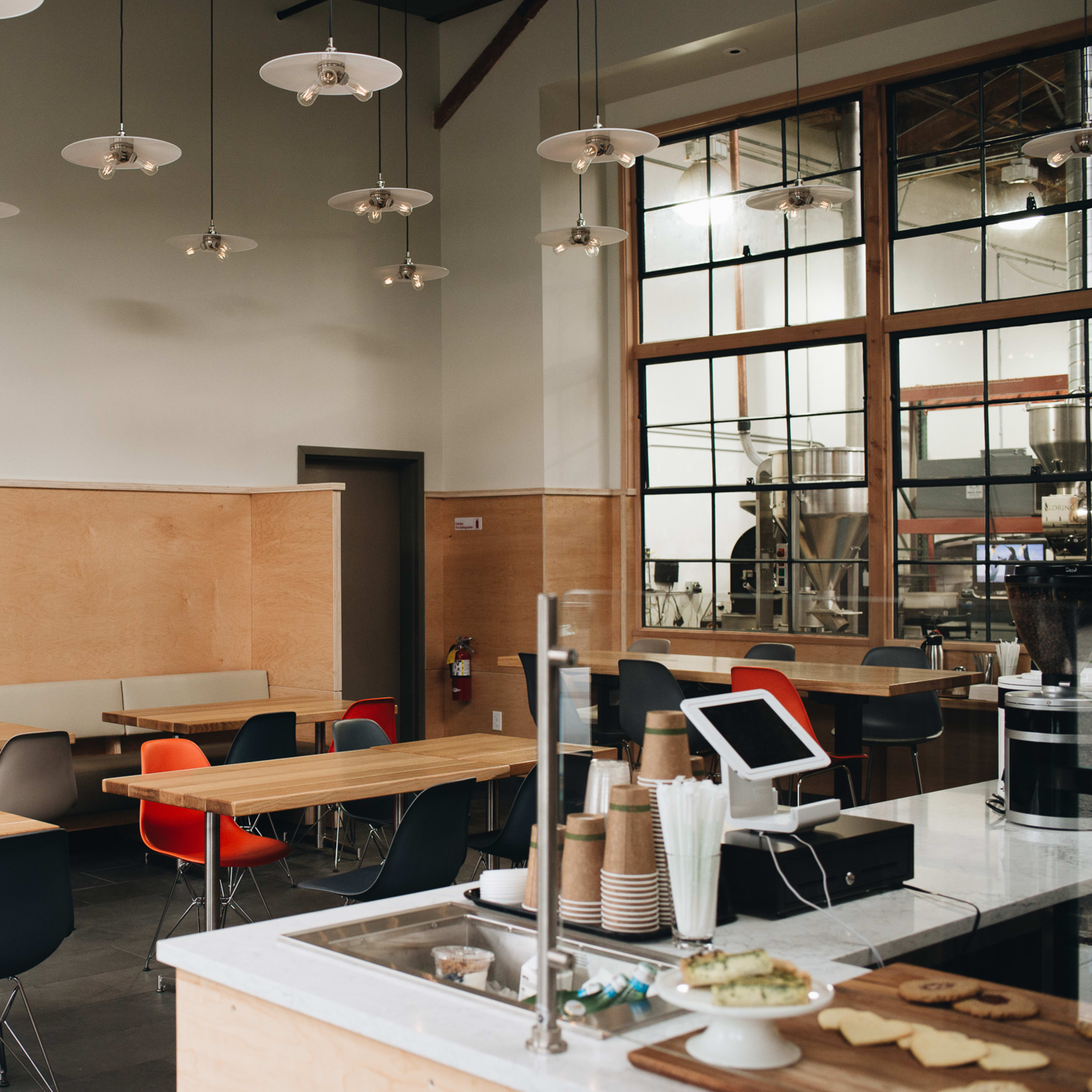 A modern café interior with wooden tables, a coffee counter, and large windows allowing natural light.