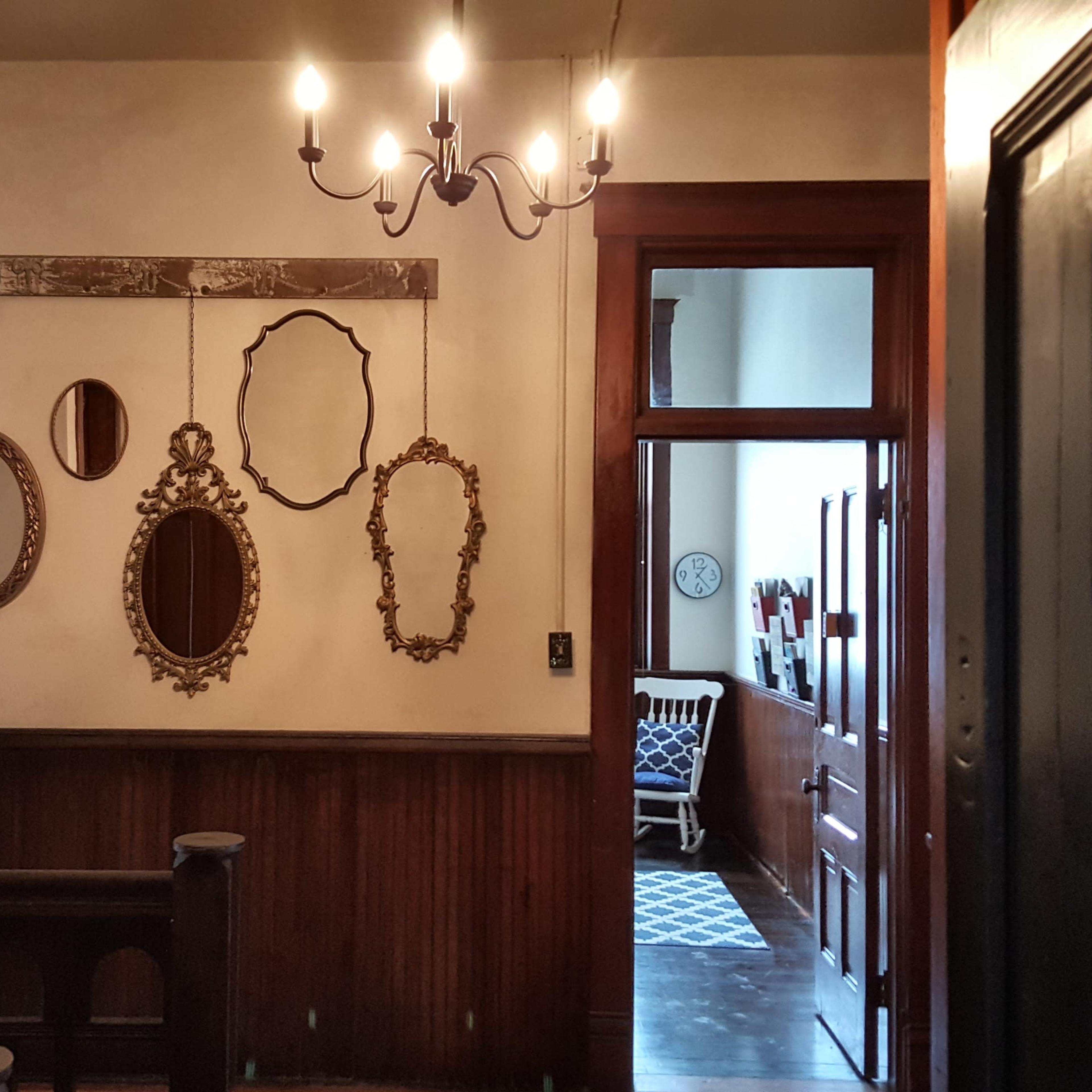 A hallway with a chandelier and several ornate mirrors mounted on the wall.